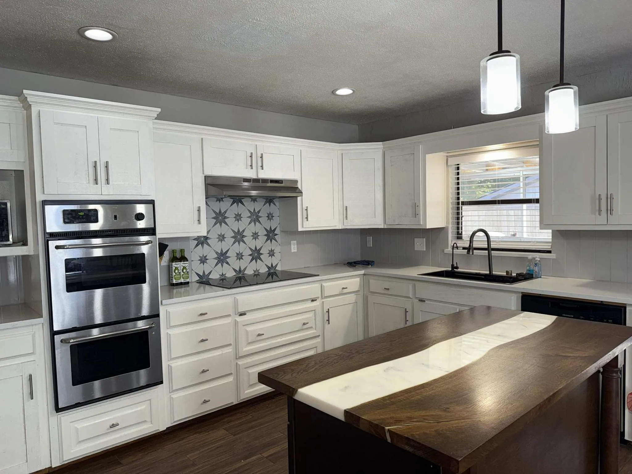 Kitchen featuring white cabinetry, stainless steel double wall oven, patterned tile backsplash, dark wood-finish flooring, and a central island with a unique inlay countertop
