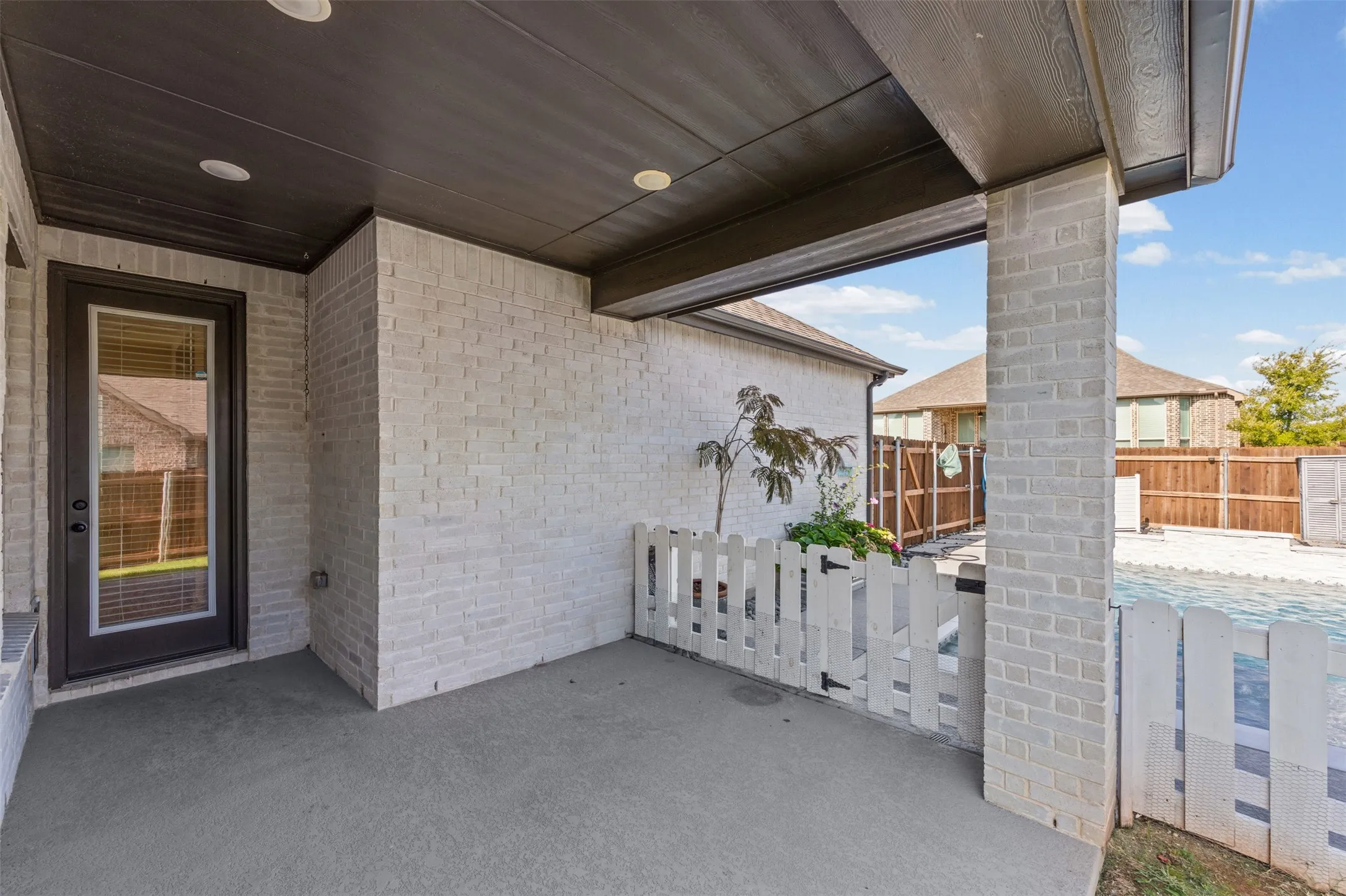 Covered patio with a dark wood-finish ceiling, recessed lighting, and light brick exterior