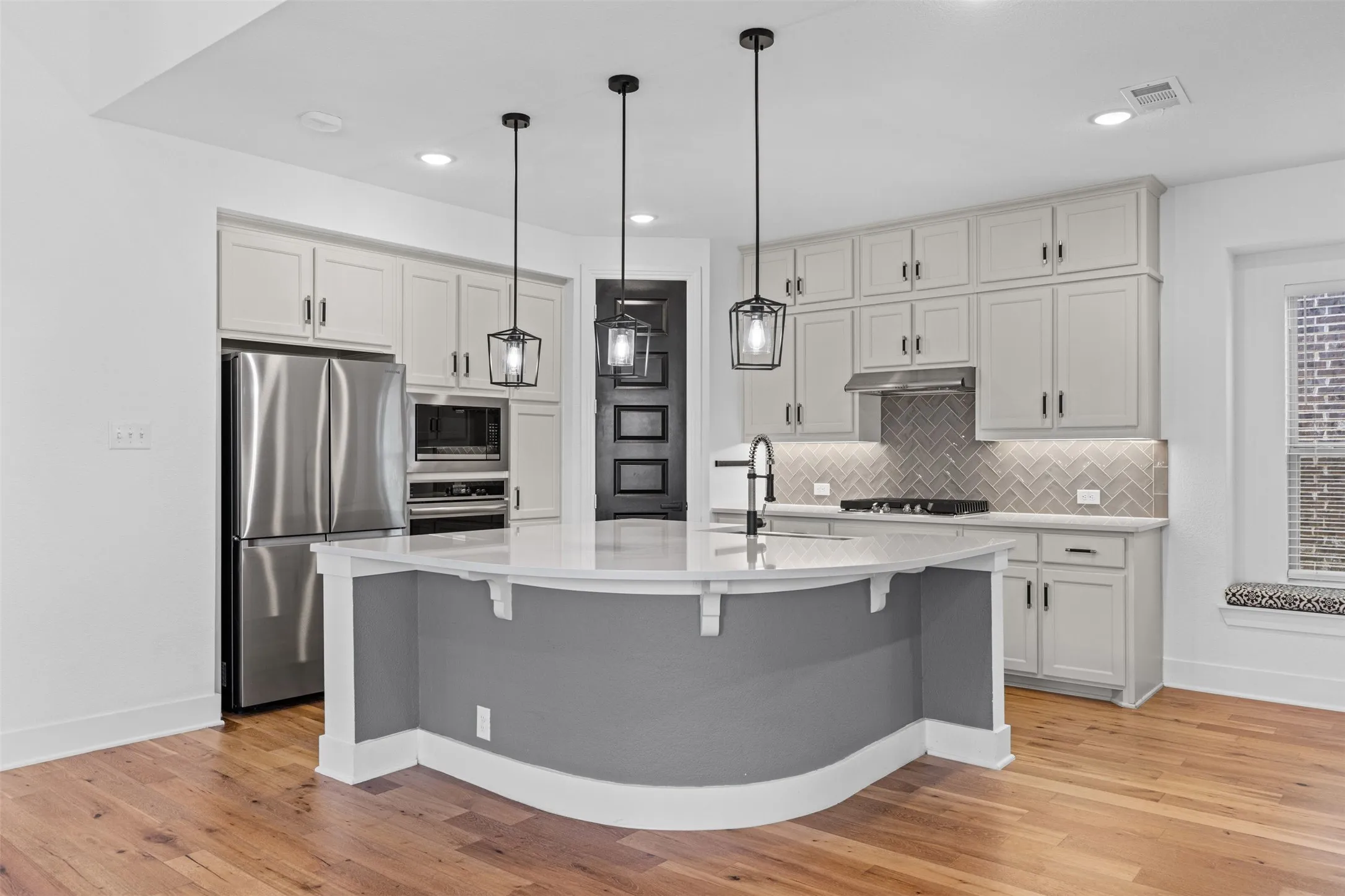 Open-concept kitchen featuring light-toned cabinetry, stainless steel appliances, a center island with a sink, pendant lighting, and wood-finish flooring