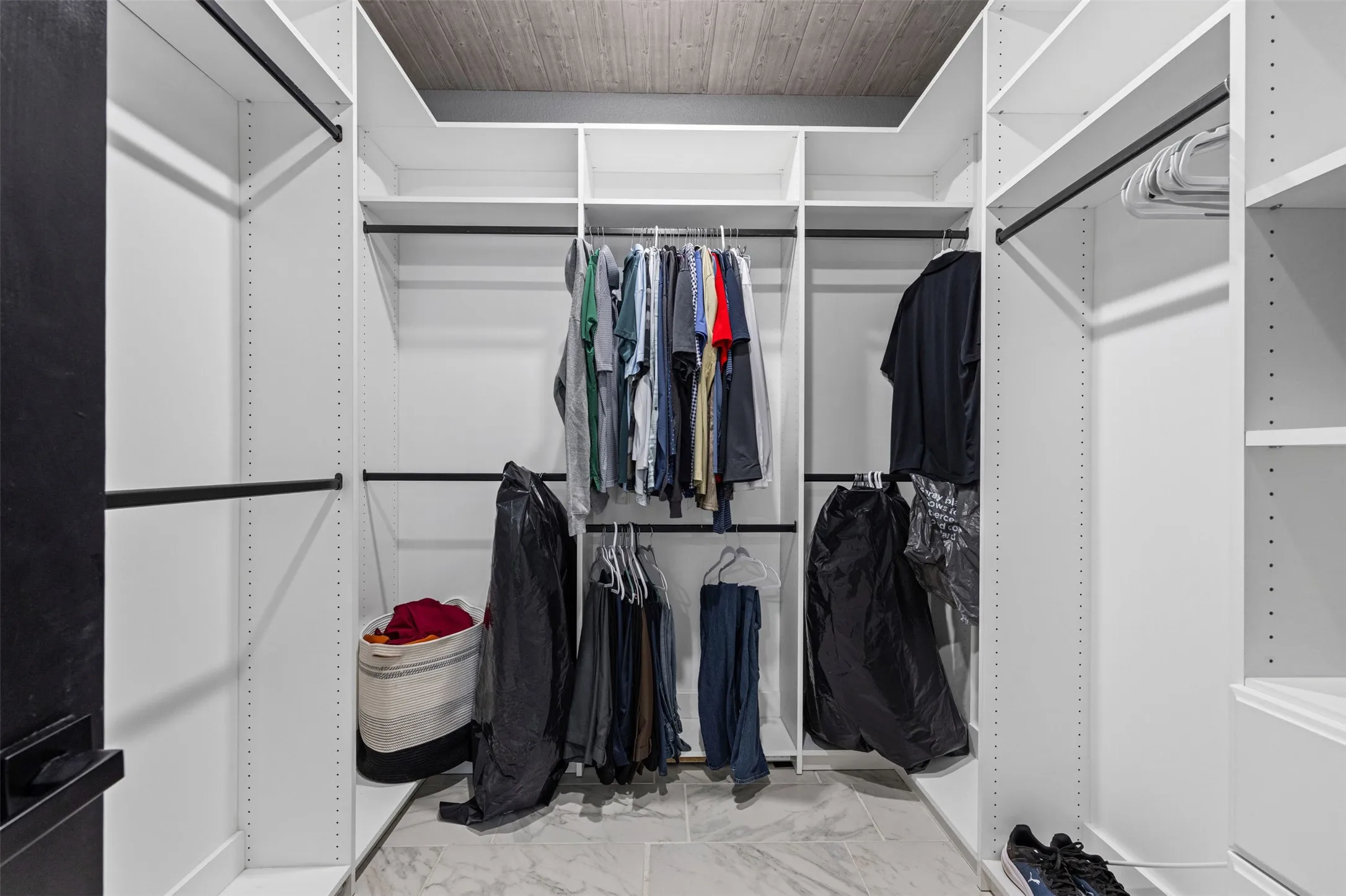 Walk-in closet with white shelving, integrated hanging rods, and light-toned tile flooring