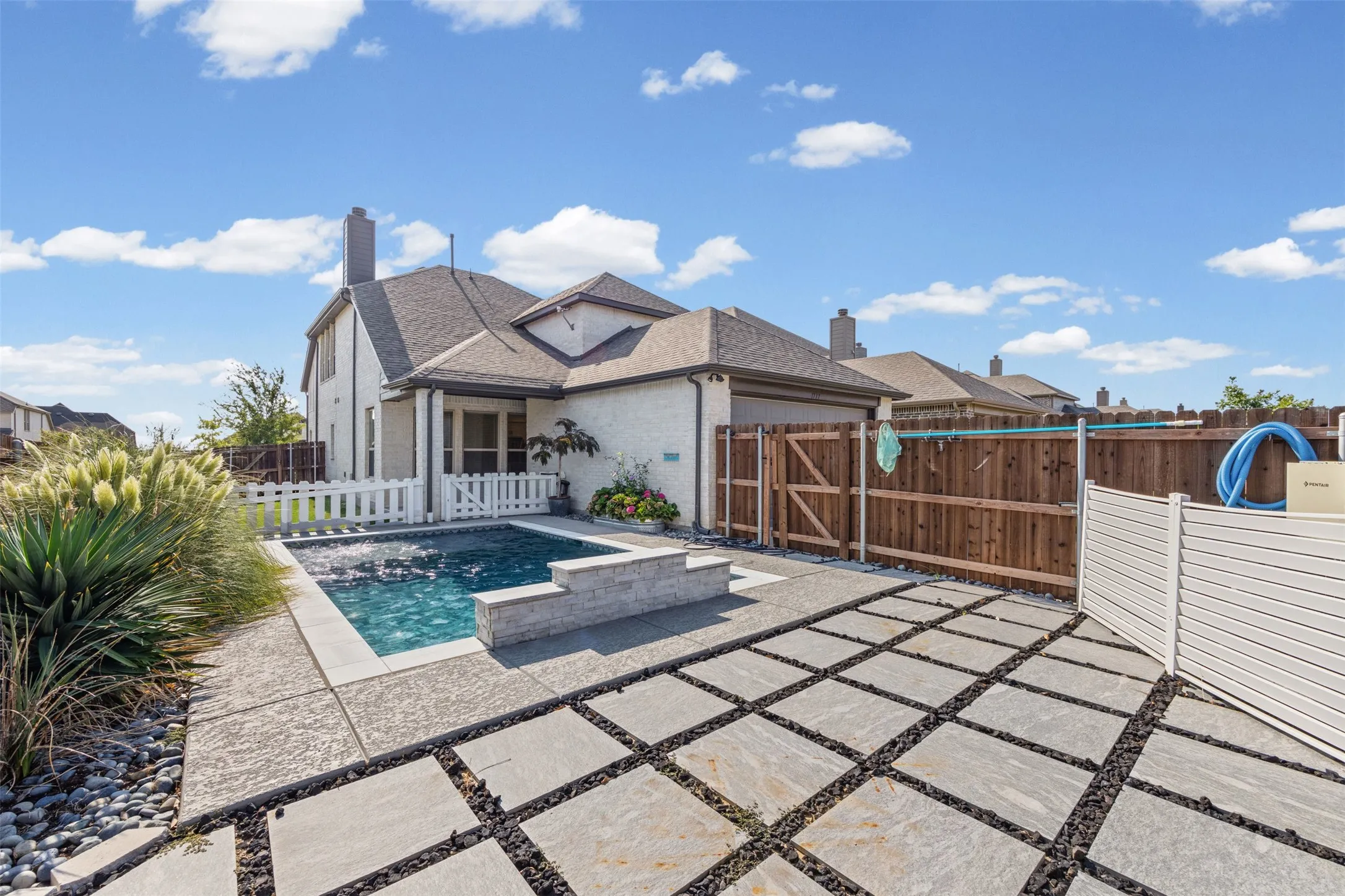 Backyard featuring a rectangular swimming pool, concrete patio, and large format paver stones set in gravel