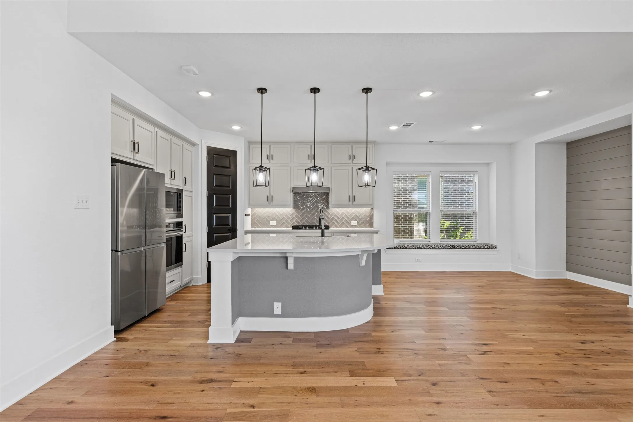 Open-concept design featuring wood-finish flooring, a kitchen island with pendant lighting, stainless steel appliances, and a window seat