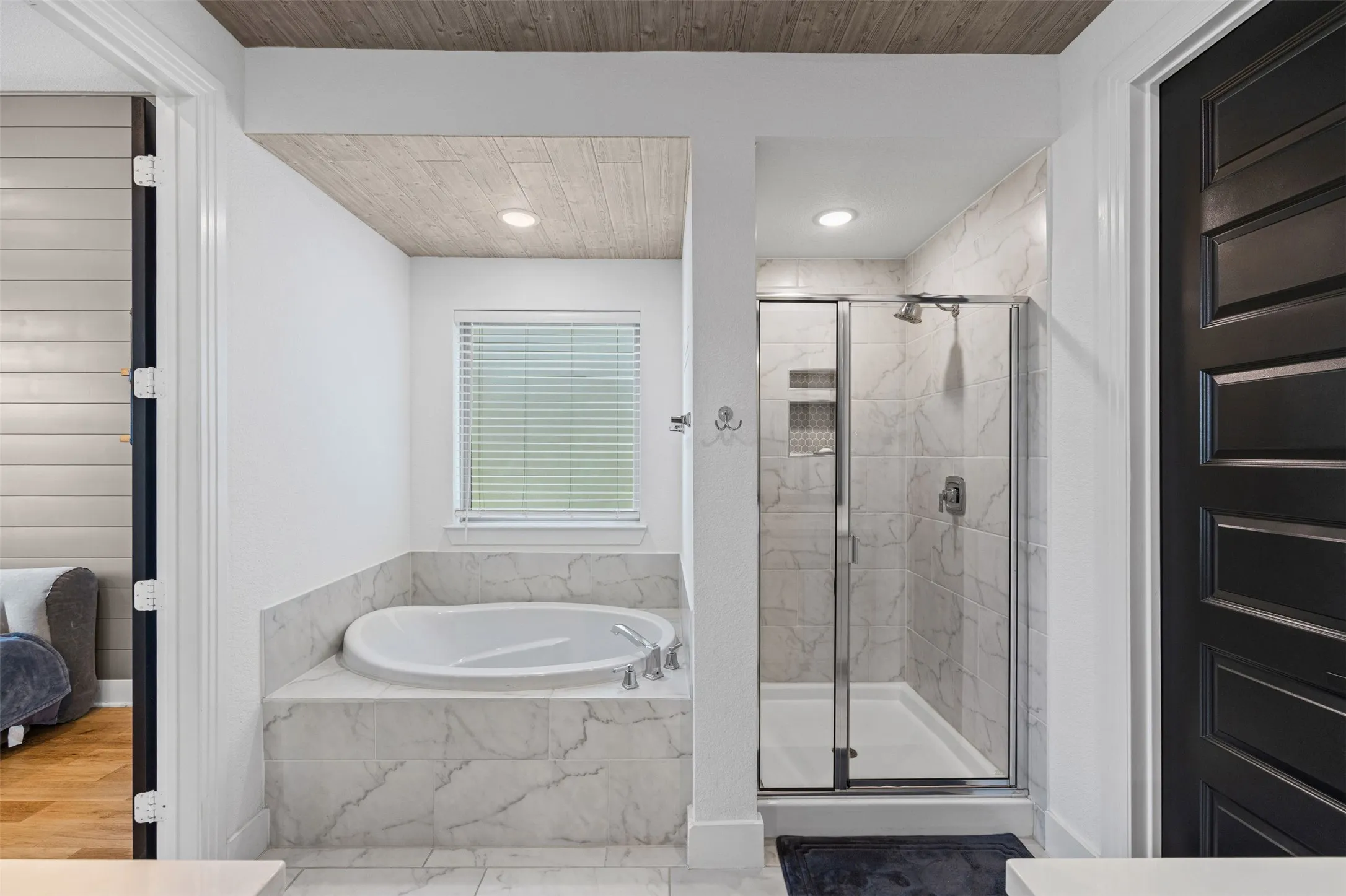 Soaking tub with a tiled surround, glass-enclosed shower with tiled walls, and wood-paneled ceiling