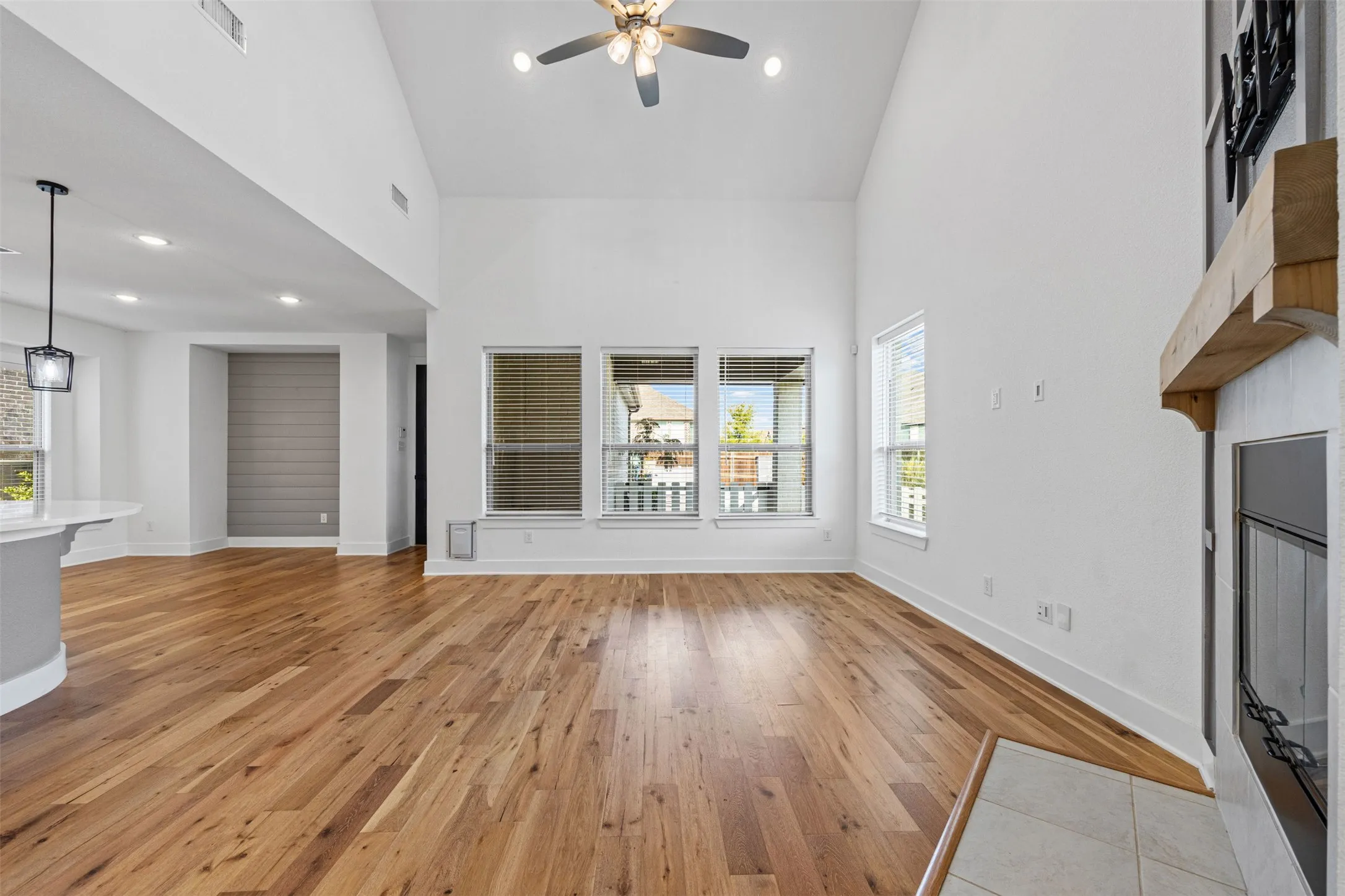 Vaulted ceiling, wood-finish flooring, ceiling fan, fireplace with wood mantel, and multiple windows