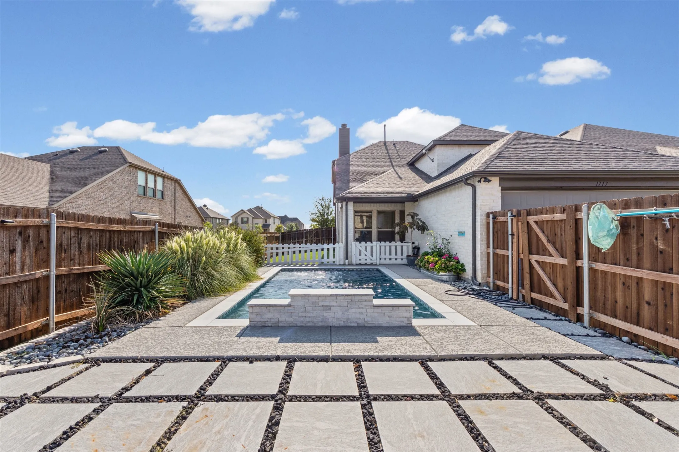 Private backyard featuring a swimming pool with a stone-clad water feature, extensive stone pavers, and a wood fence