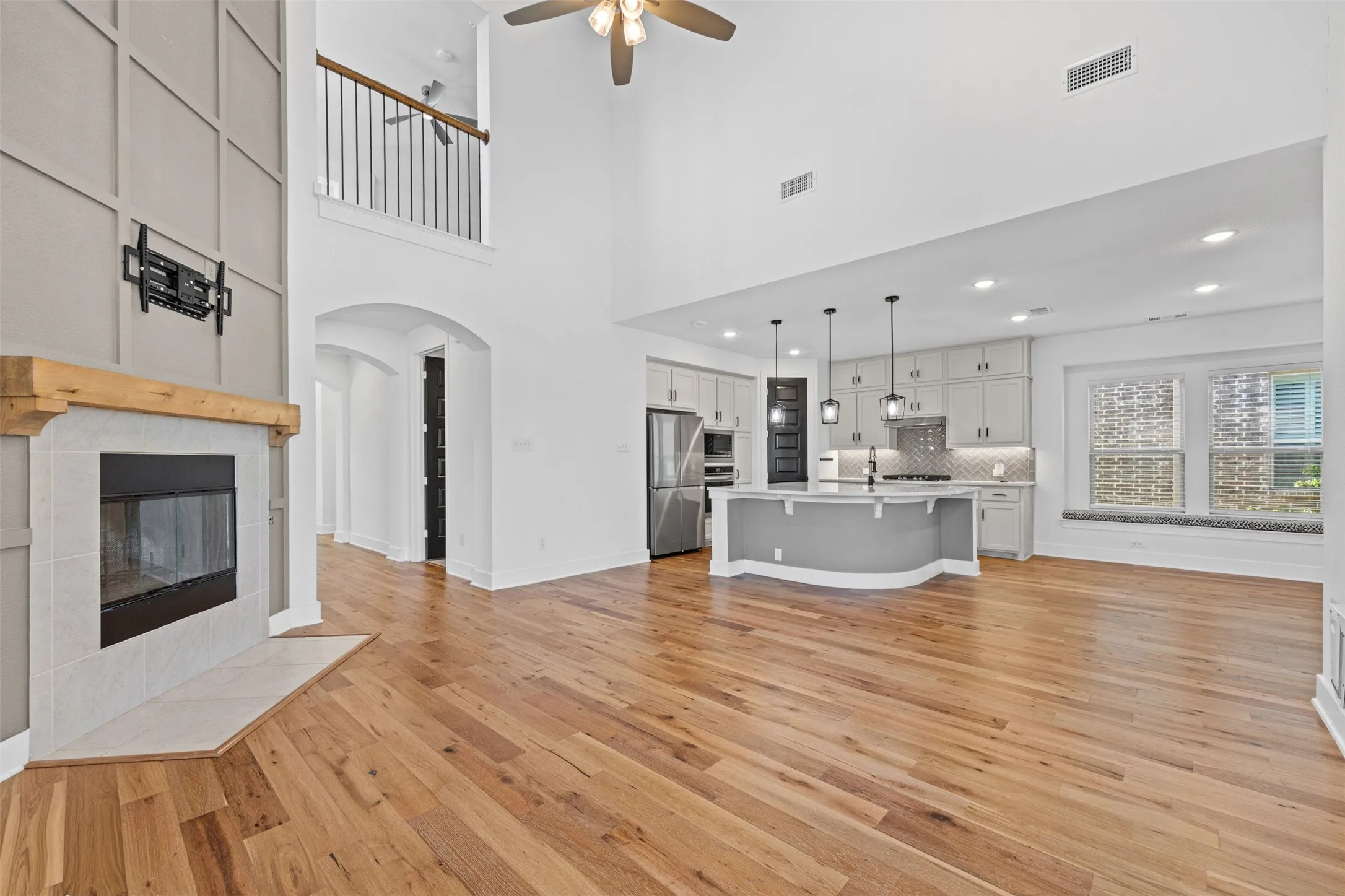 Vaulted ceiling, wood-finish flooring, fireplace with wood mantel, kitchen island with pendant lighting, and built-in window seating