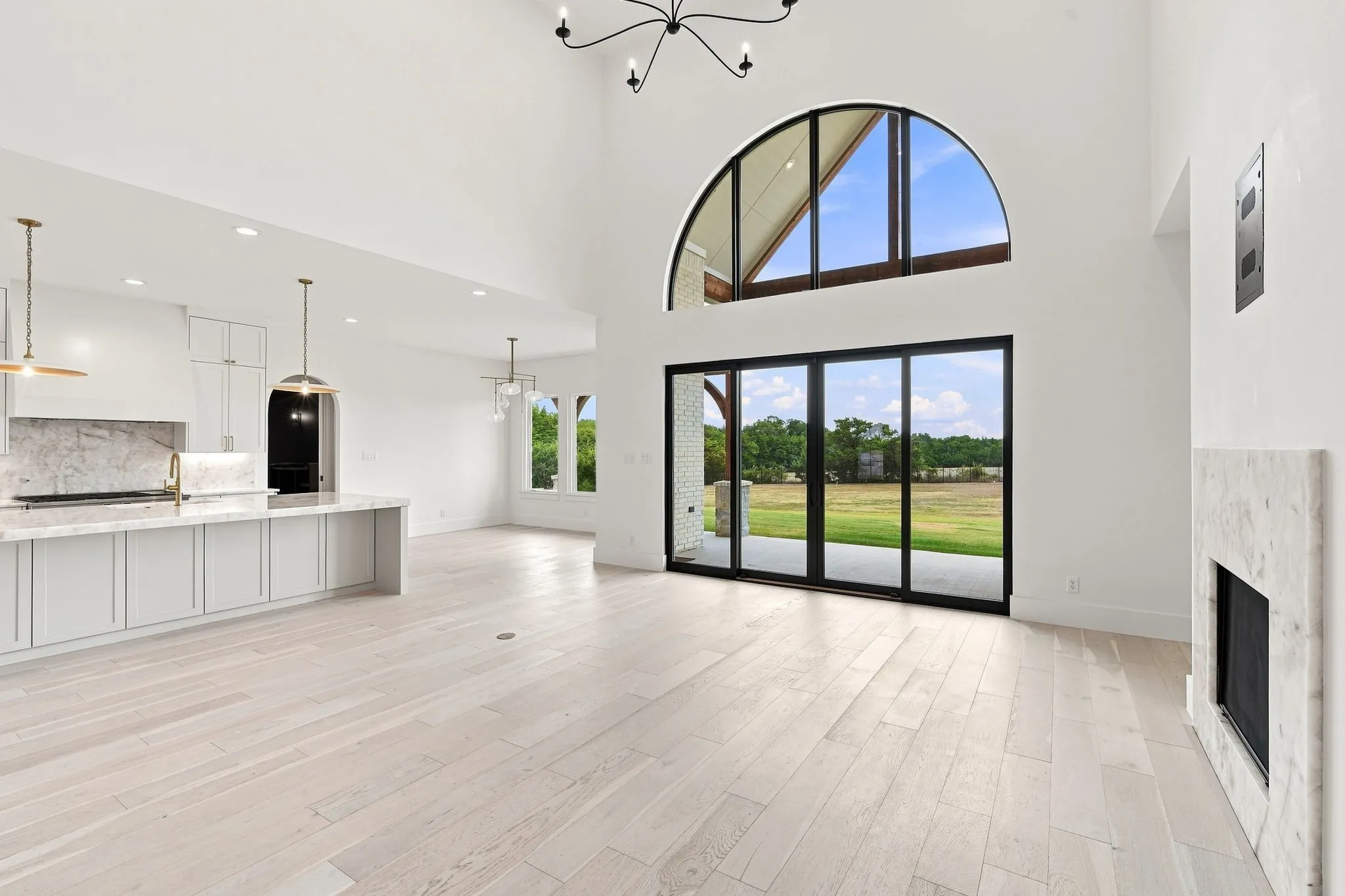 Bright, open-concept living space anchored by expansive glass doors and arched transom window overlooking manicured grounds