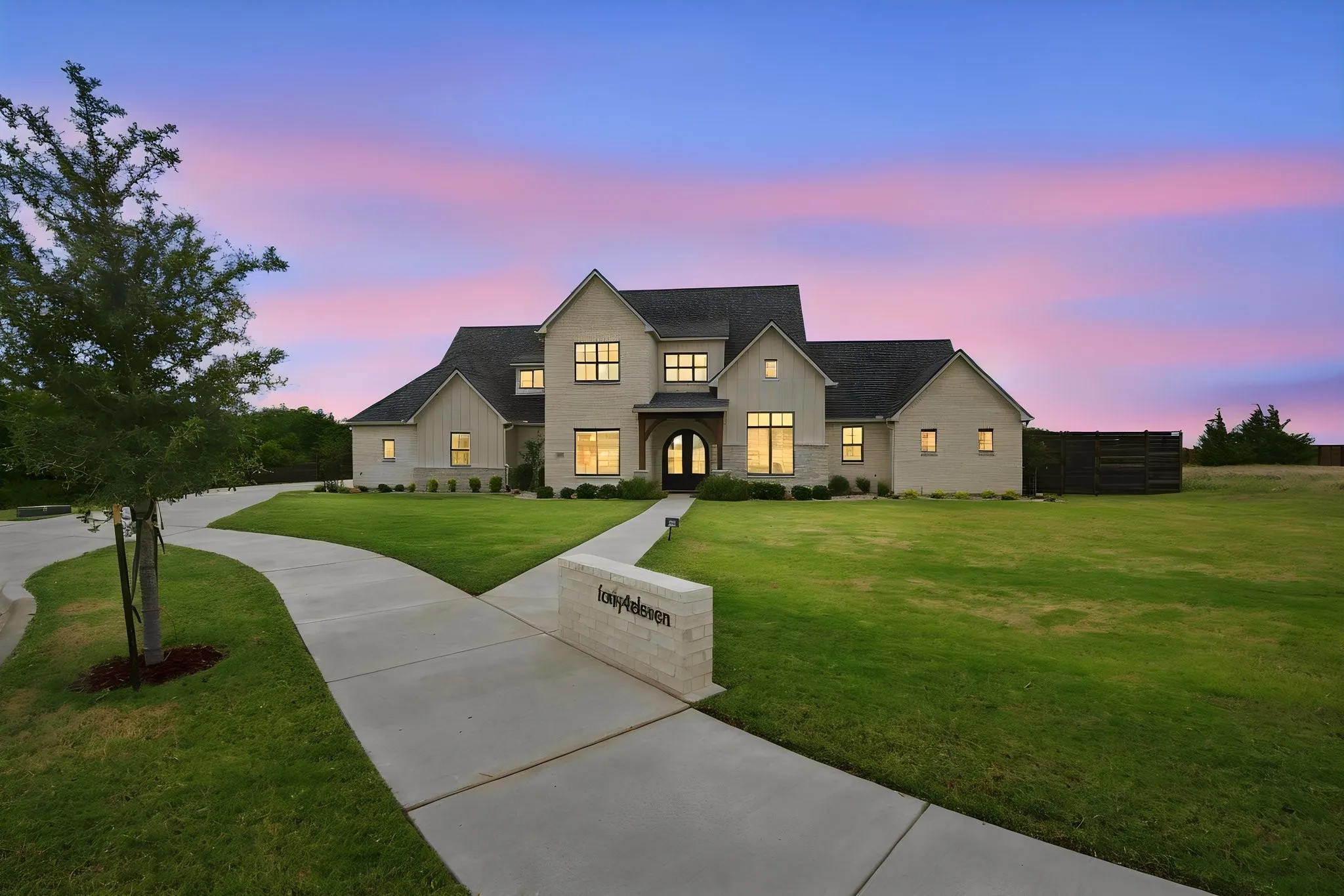 Elegant two-story residence featuring a cream-colored exterior with dark architectural accents, multiple gabled rooflines, and illuminated windows throughout