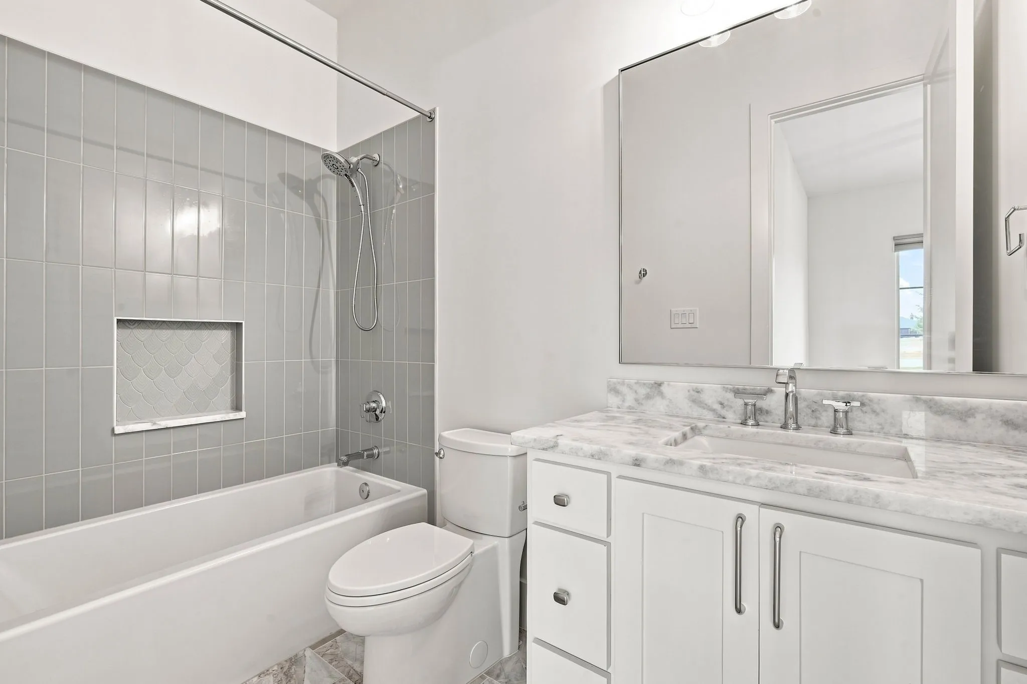 Spa-inspired bathroom featuring a marble-look vanity countertop with dual sink configuration, white cabinetry with polished hardware, and a frameless mirror with integrated lighting