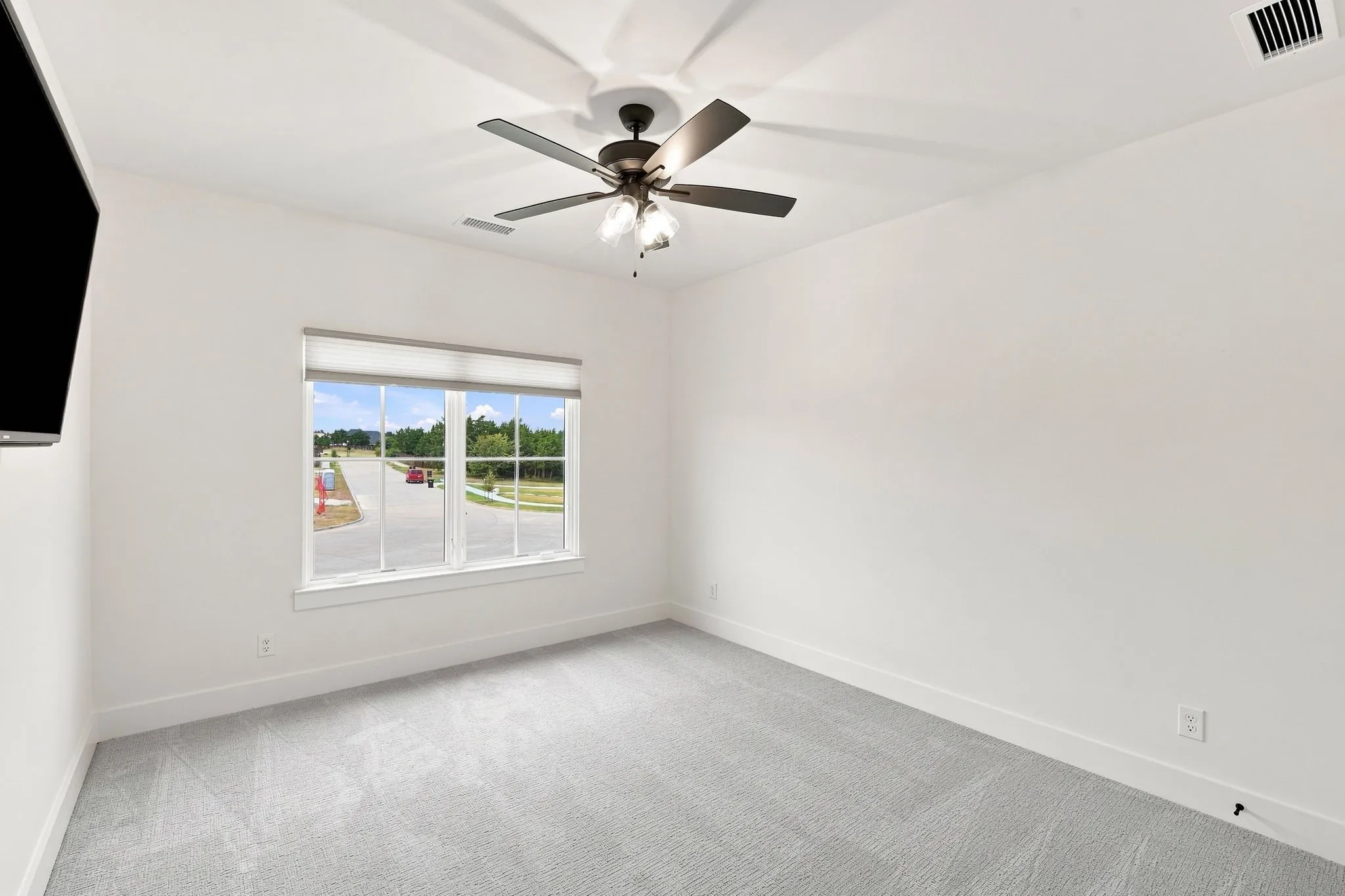White walls, light gray carpet, window with roller shades, and a ceiling fan with integrated lighting
