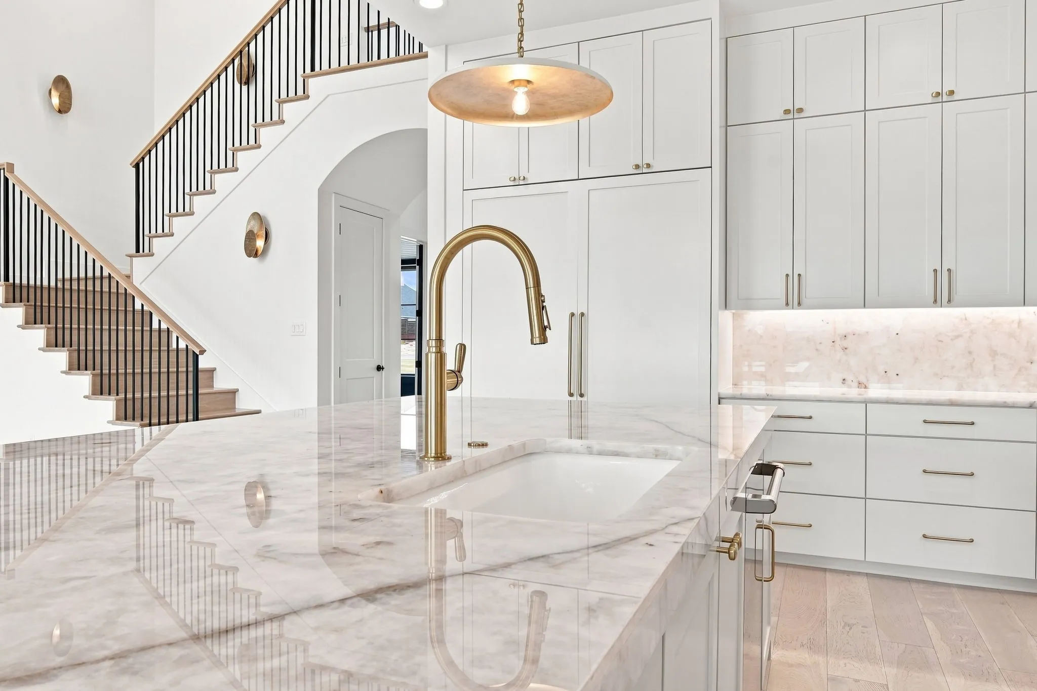 Spa-inspired primary bathroom featuring a freestanding soaking tub, polished stone flooring, white shaker cabinetry with brushed brass hardware, and a brass pendant light fixture