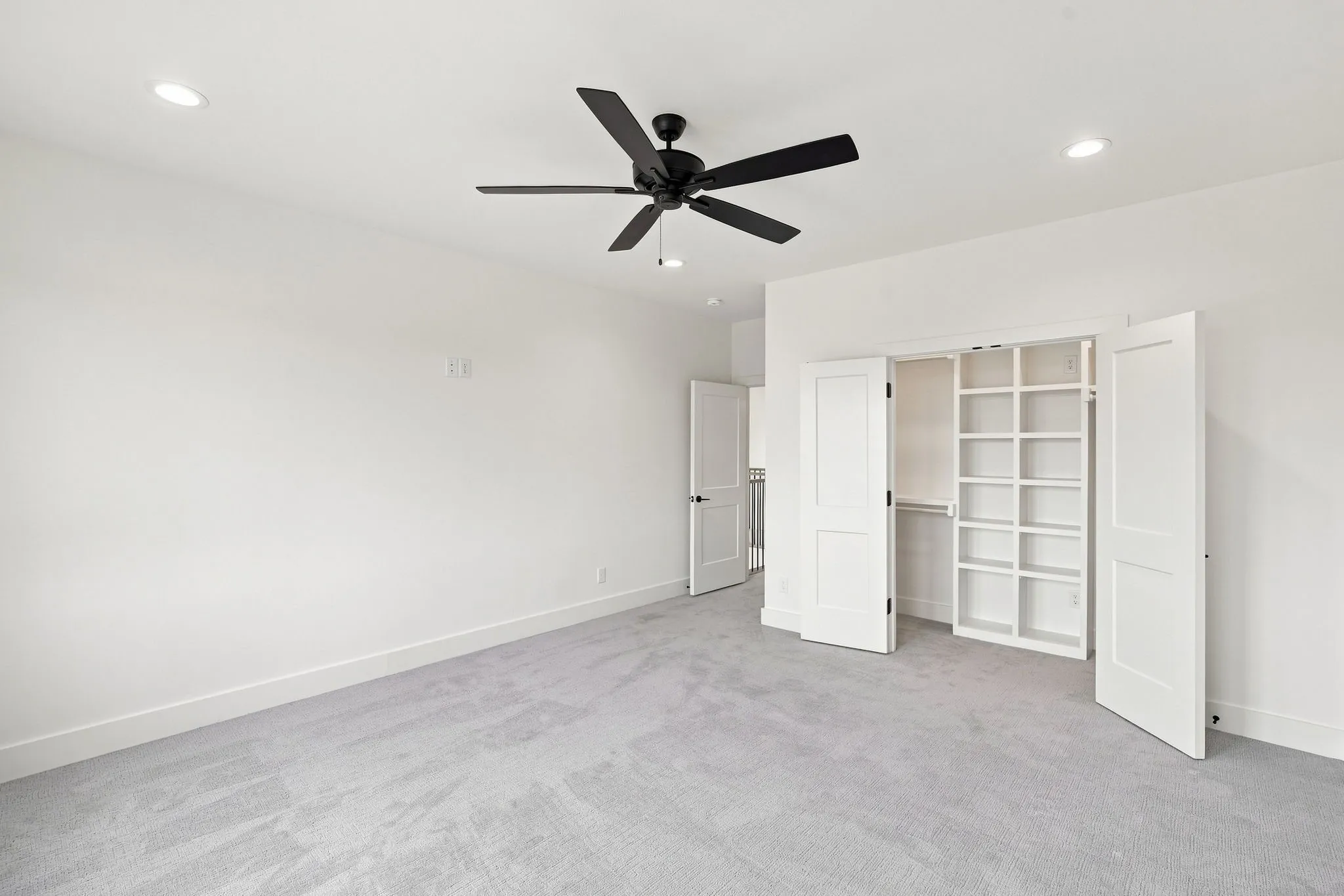 Spacious primary room featuring recessed ceiling lighting, a contemporary ceiling fan with integrated light fixture, and built-in shelving with multiple display cubbies