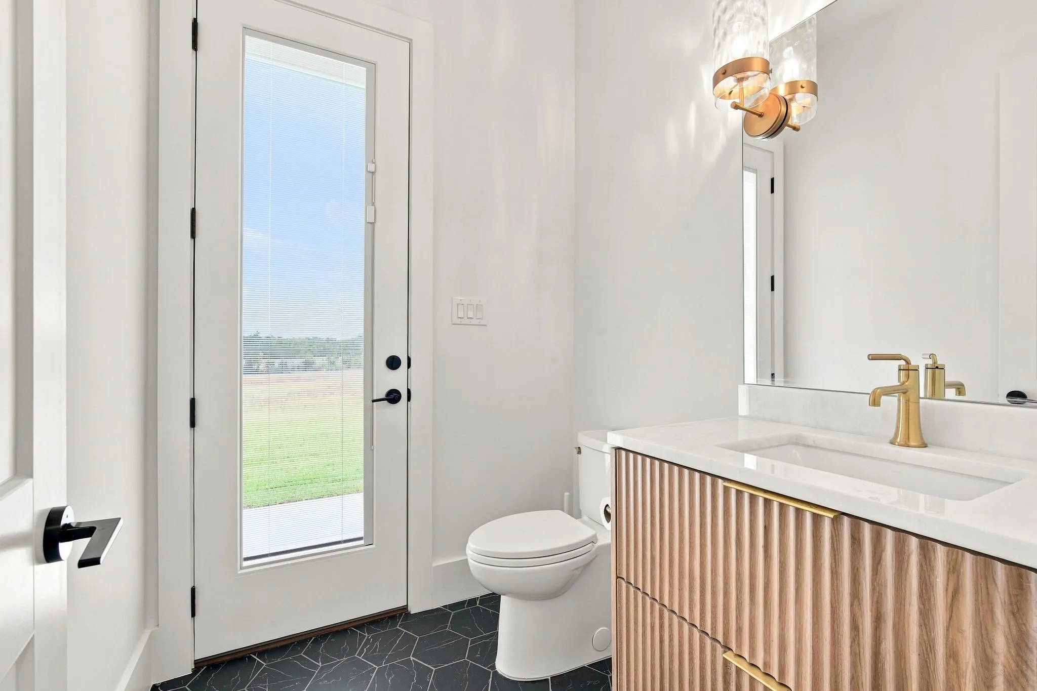 Modern bathroom featuring a wood-finish vanity with integrated sink and quartz countertop, brass faucet fixture, and dark tile flooring