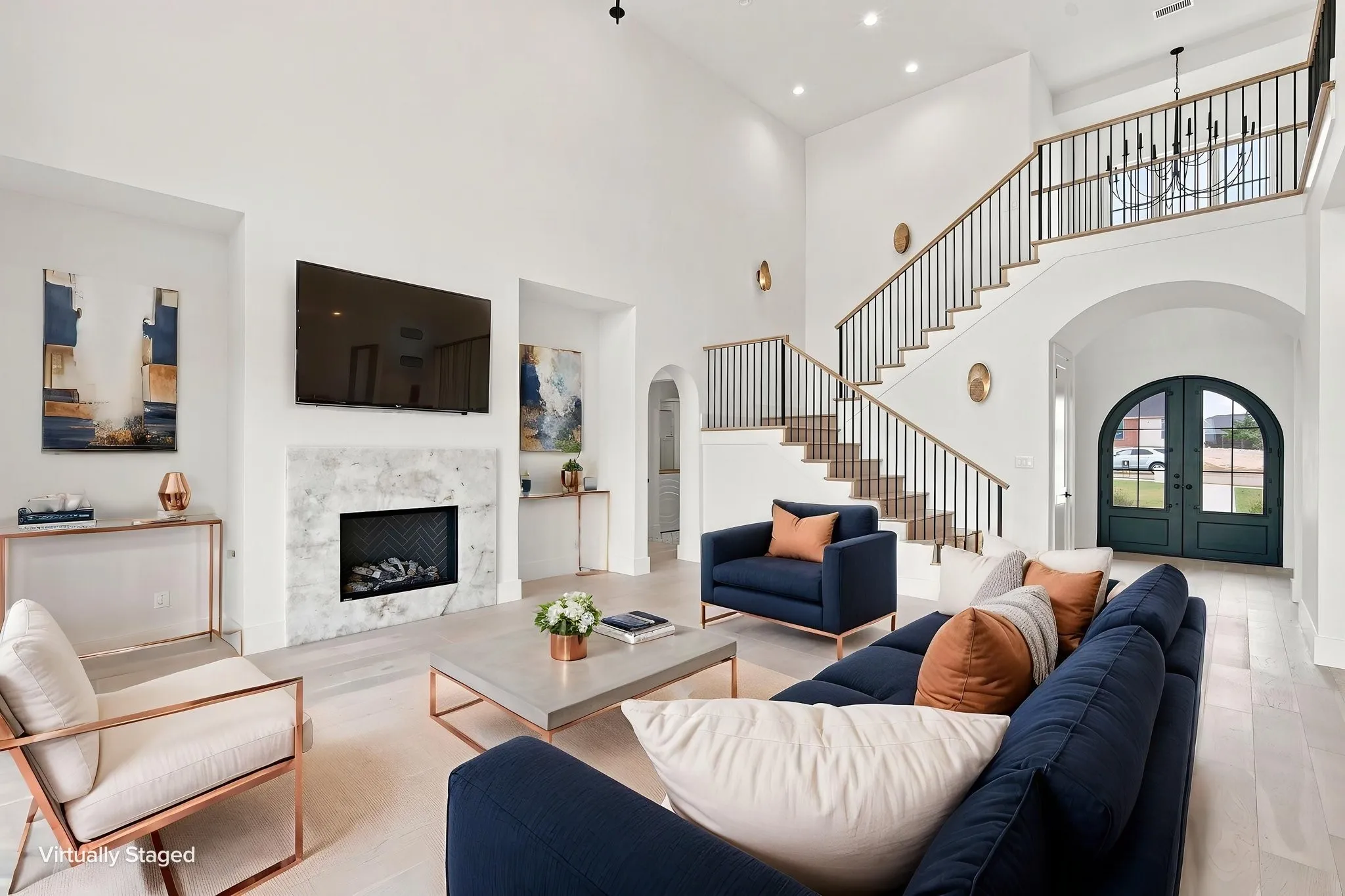 Sophisticated two-story living space featuring soaring ceilings, a curved staircase with metal railings, and an open floor plan anchored by a fireplace with stone surround
