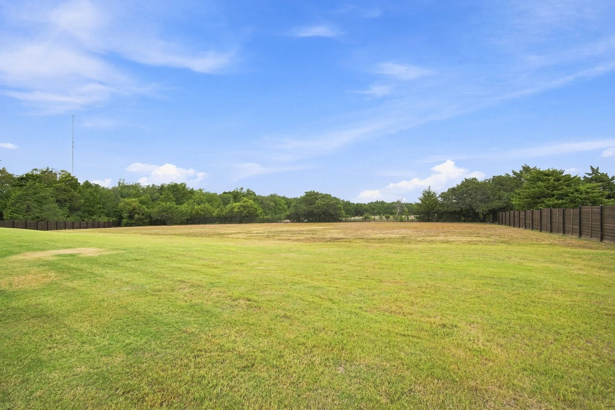 Expansive grounds featuring a manicured lawn with mature tree lines on both sides and a secure perimeter fence