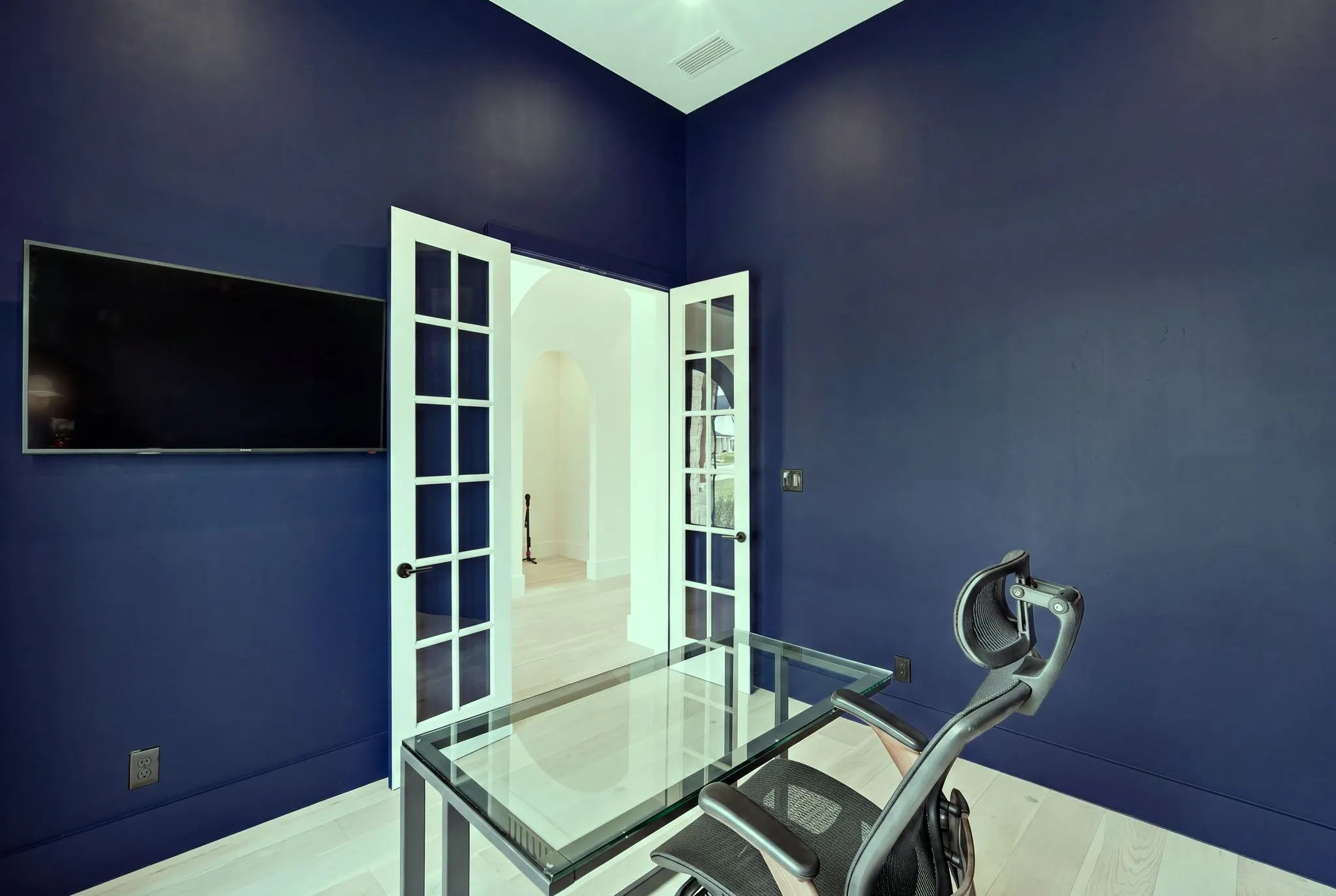 Modern home office featuring deep navy walls, recessed ceiling lighting, and glass French doors with grid-pane detailing
