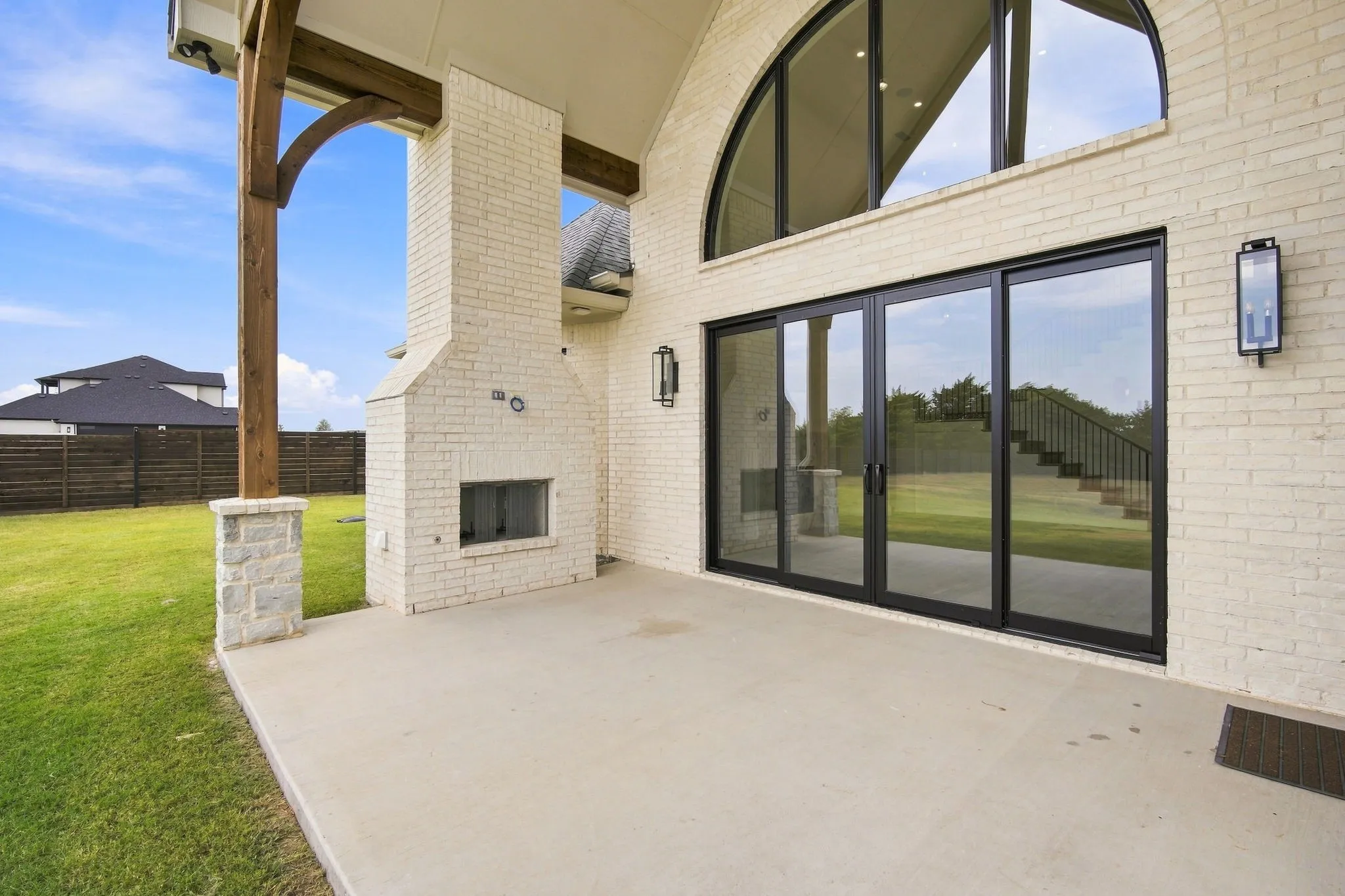 Expansive covered patio with concrete flooring and overhead beam structure, framed by white brick exterior and black-framed sliding glass doors