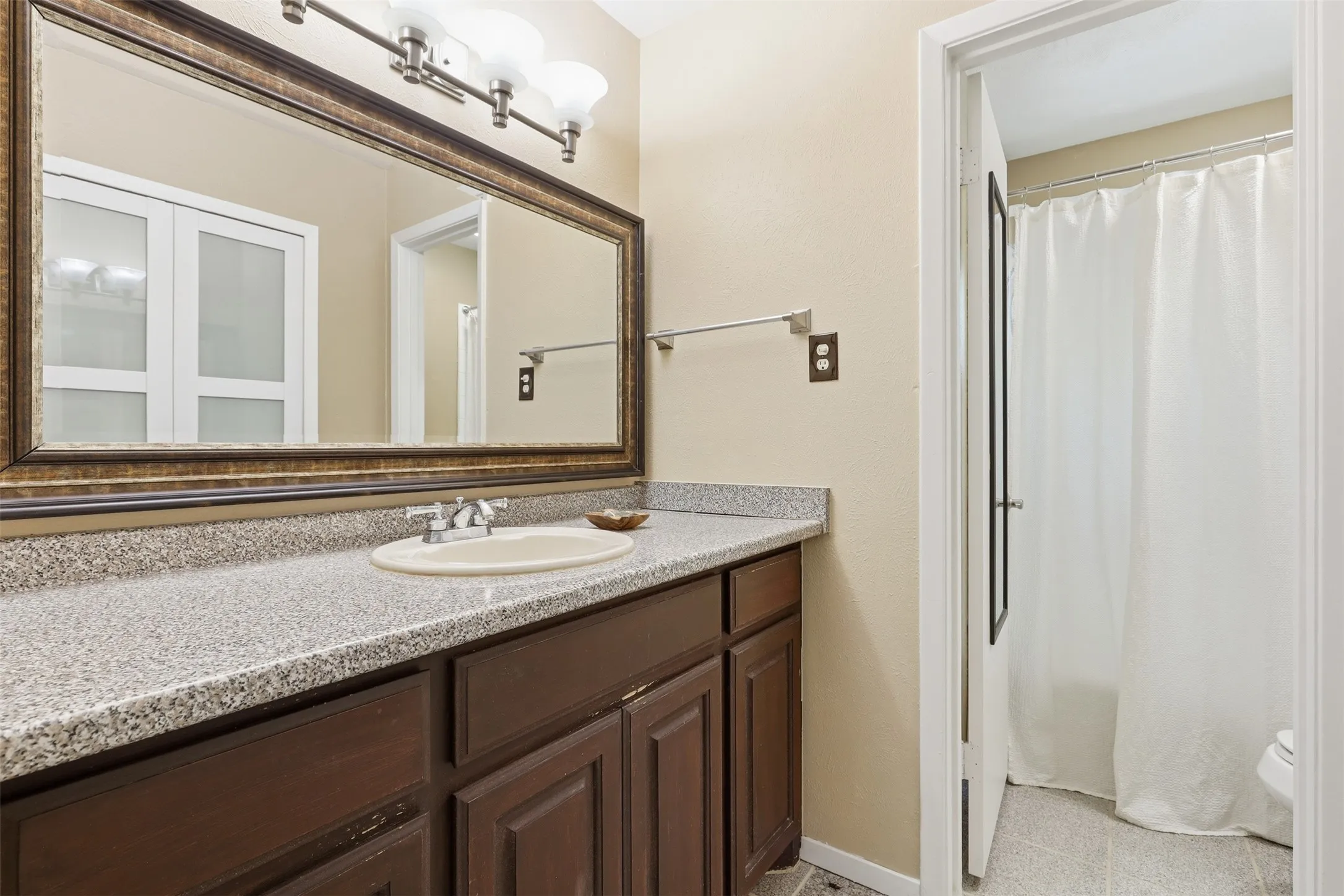 Functional bathroom vanity area featuring generous counter space, dark wood cabinetry, a large mirror, and built-in linen storage