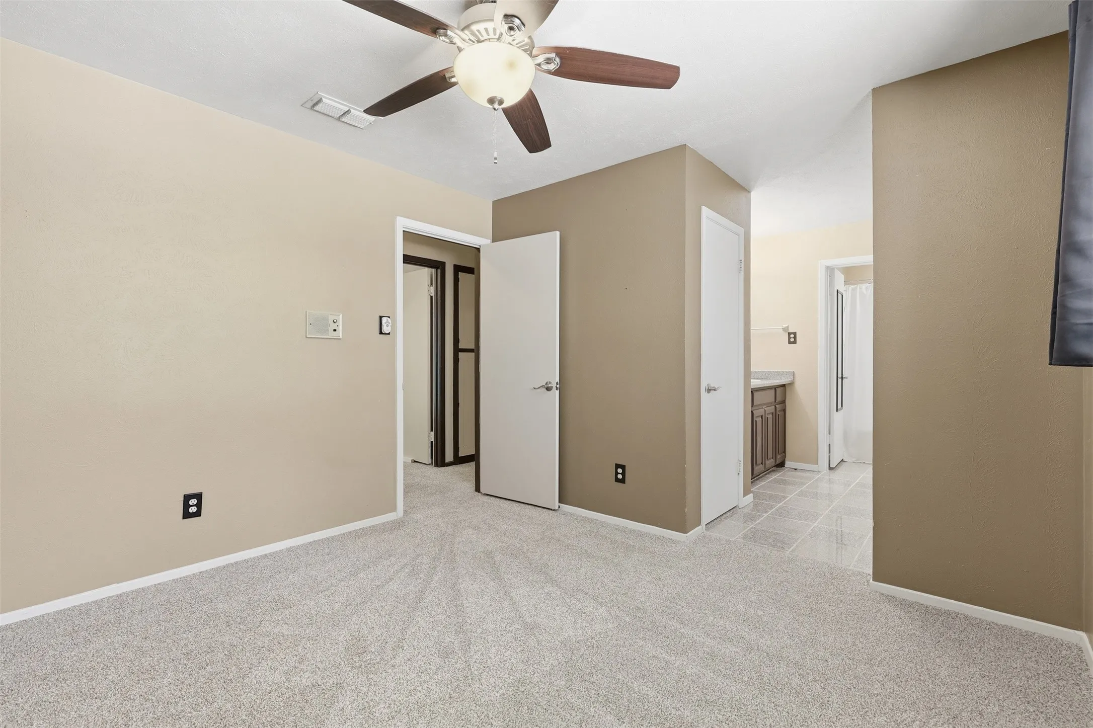 Additional view of the primary bedroom highlighting its ceiling fan, neutral colors, new carpet, and direct access to the adjoining bathroom area