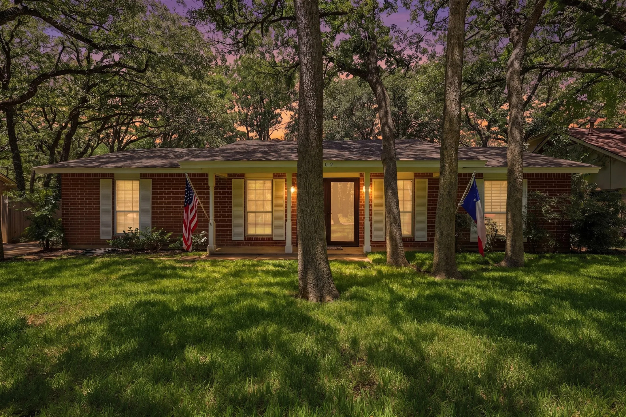 Twilight view of this inviting single-story Woodland West home, showcasing warm exterior lighting, mature trees, and classic brick architecture