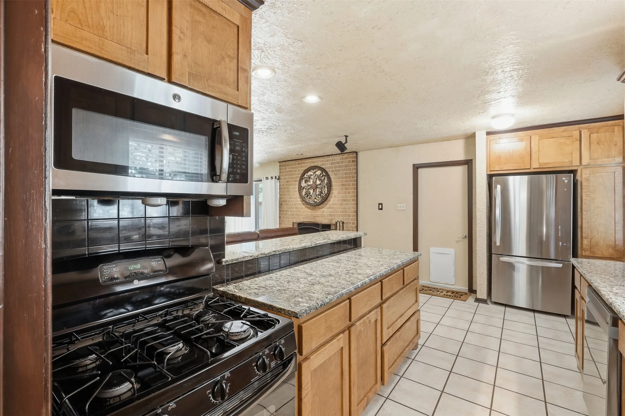 Kitchen with gas range, built-in microwave, granite counters, ample cabinetry, and a raised breakfast bar overlooking the living room fireplace
