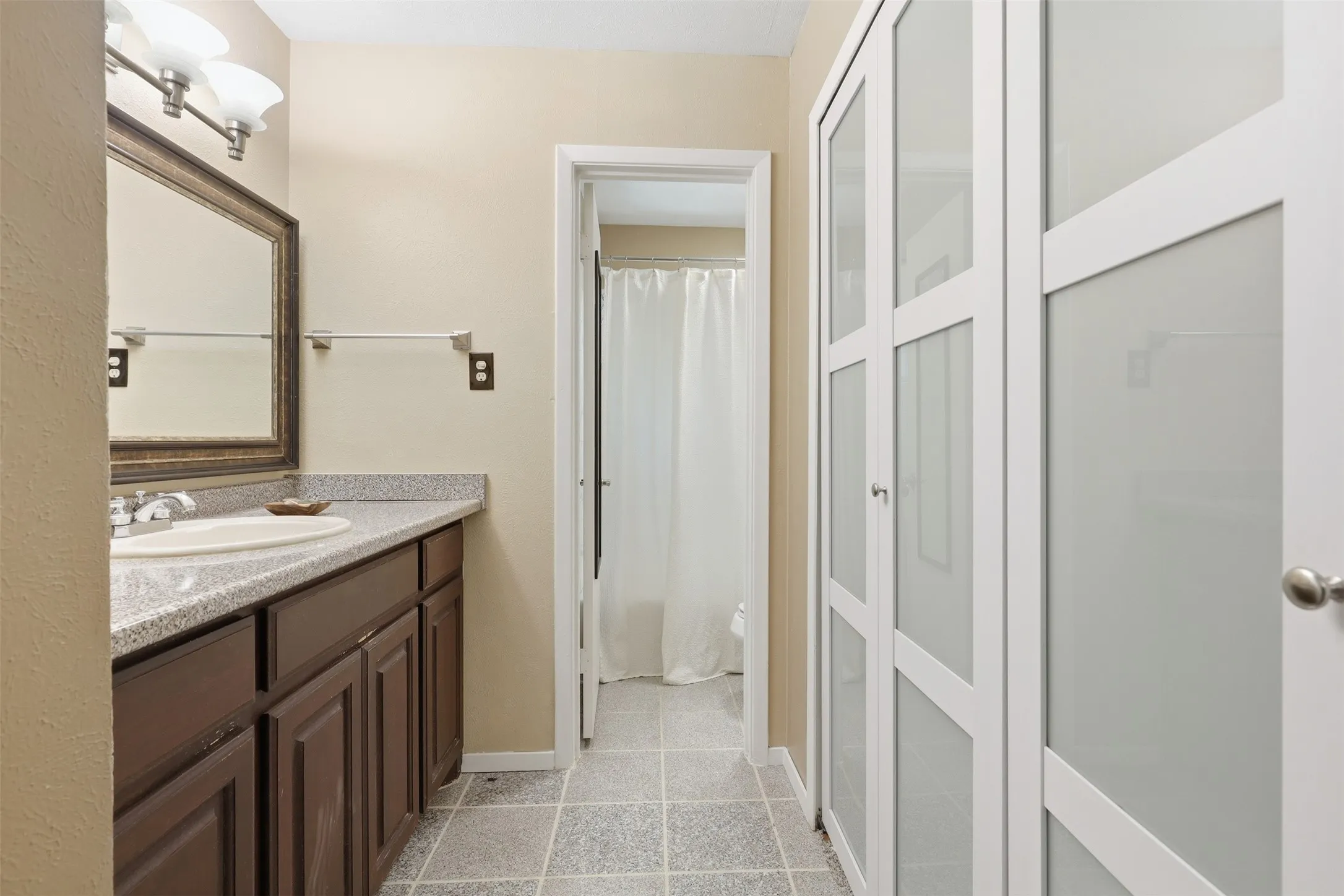 Dressing and vanity area with ample built-in storage, tile flooring, and access to the separate tub-and-shower room. New Closet Doors (7/2026)