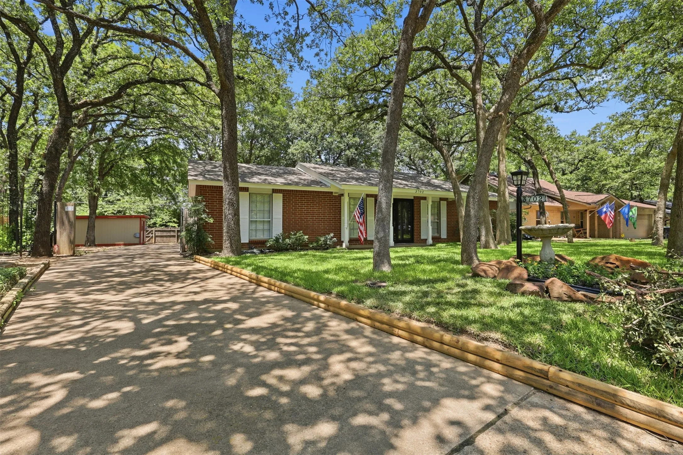Charming single-story brick home in Arlington, TX 76013, surrounded by mature shade trees with an extended driveway leading to the attached garage