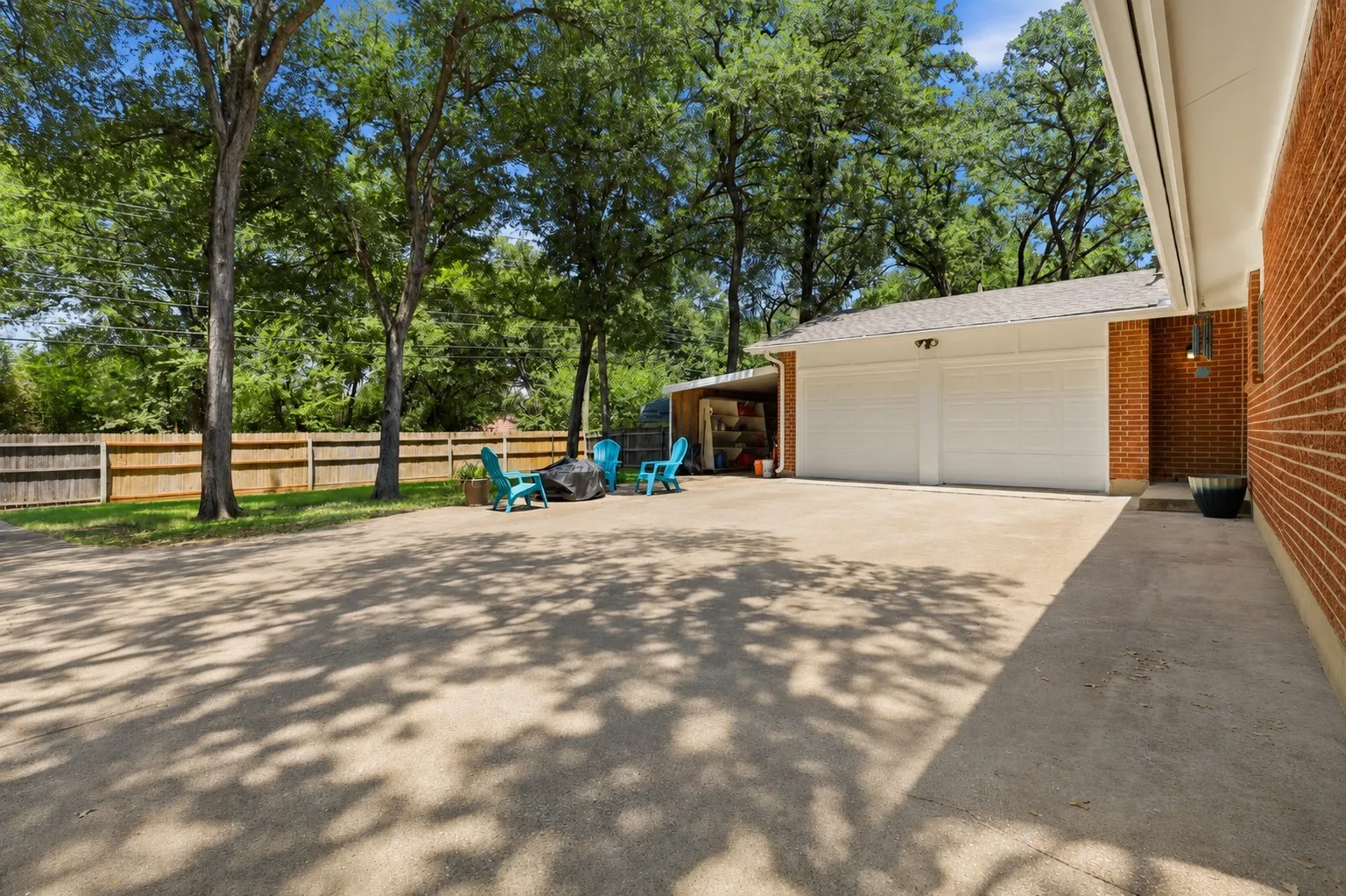 Expansive backyard patio and driveway provide abundant outdoor living space beneath mature shade trees, with convenient access to the attached two-car garage