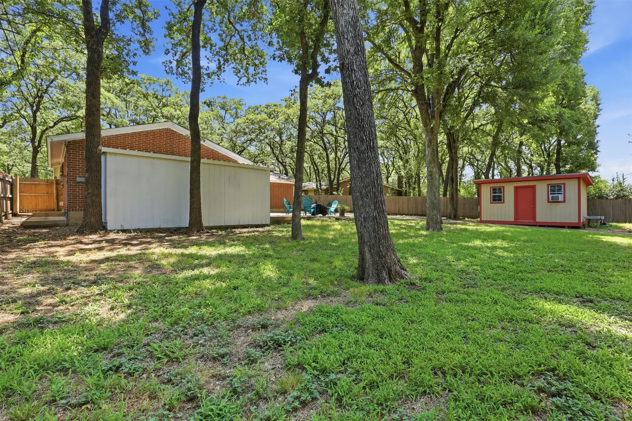 Spacious fenced backyard with a large patio, mature trees, attached two-car garage, and covered storage area in Arlington’s Woodland West neighborhood