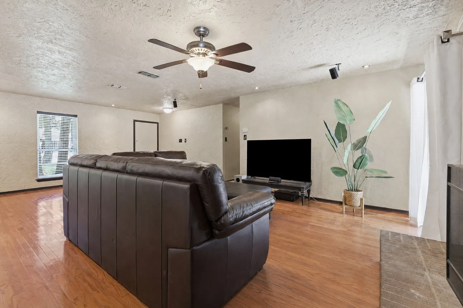 Spacious living room centered around a brick fireplace, with wood flooring, abundant lighting, and access to the backyard patio