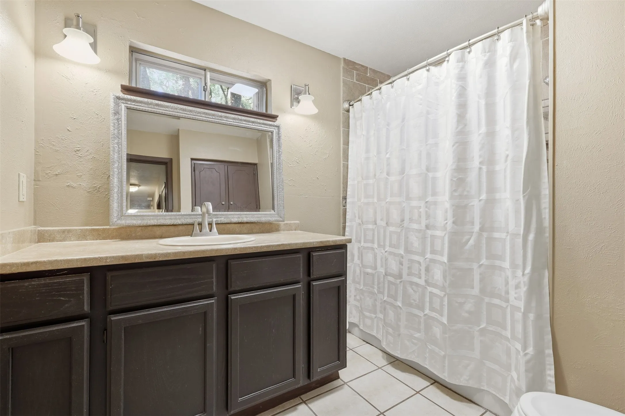 Full bathroom with a spacious vanity, decorative mirror, tile flooring, window, and tub-and-shower combination