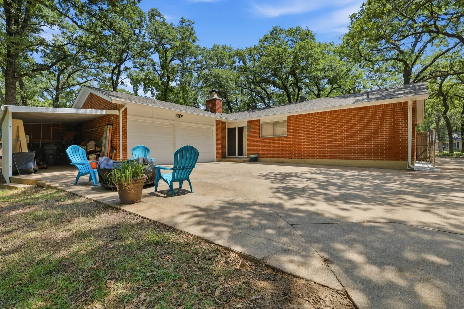 Expansive backyard patio and driveway provide abundant outdoor living space beneath mature shade trees, with convenient access to the attached two-car garage