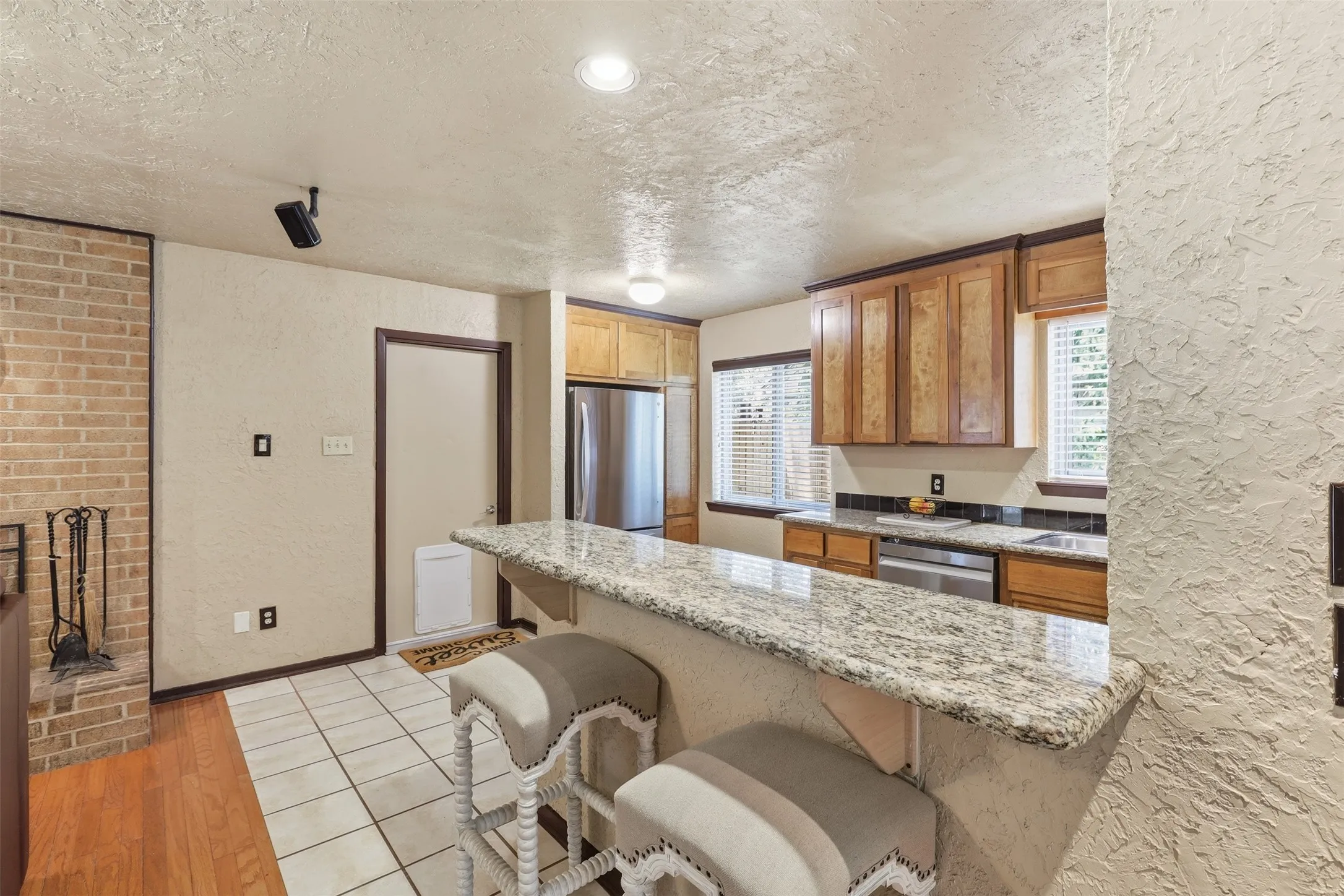 Functional galley kitchen with granite countertops, plentiful cabinet storage, stainless-steel dishwasher, tile flooring, and an adjacent dining area