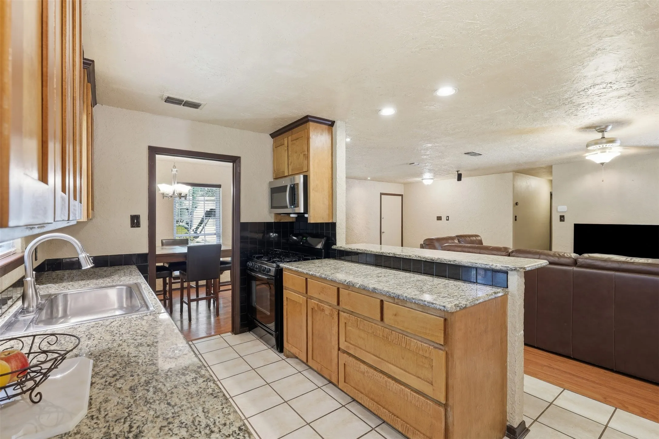 Galley-style kitchen with granite countertops, wood cabinetry, double sink, tile flooring, and multiple windows.