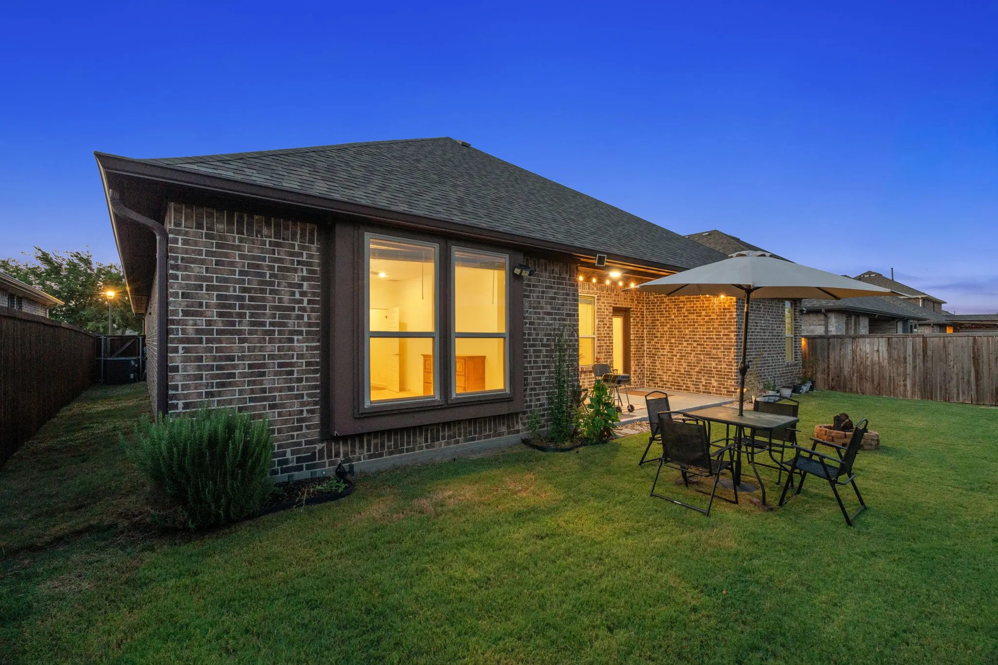 Expansive backyard featuring a manicured lawn, brick exterior, private fencing, an outdoor patio, and string lighting