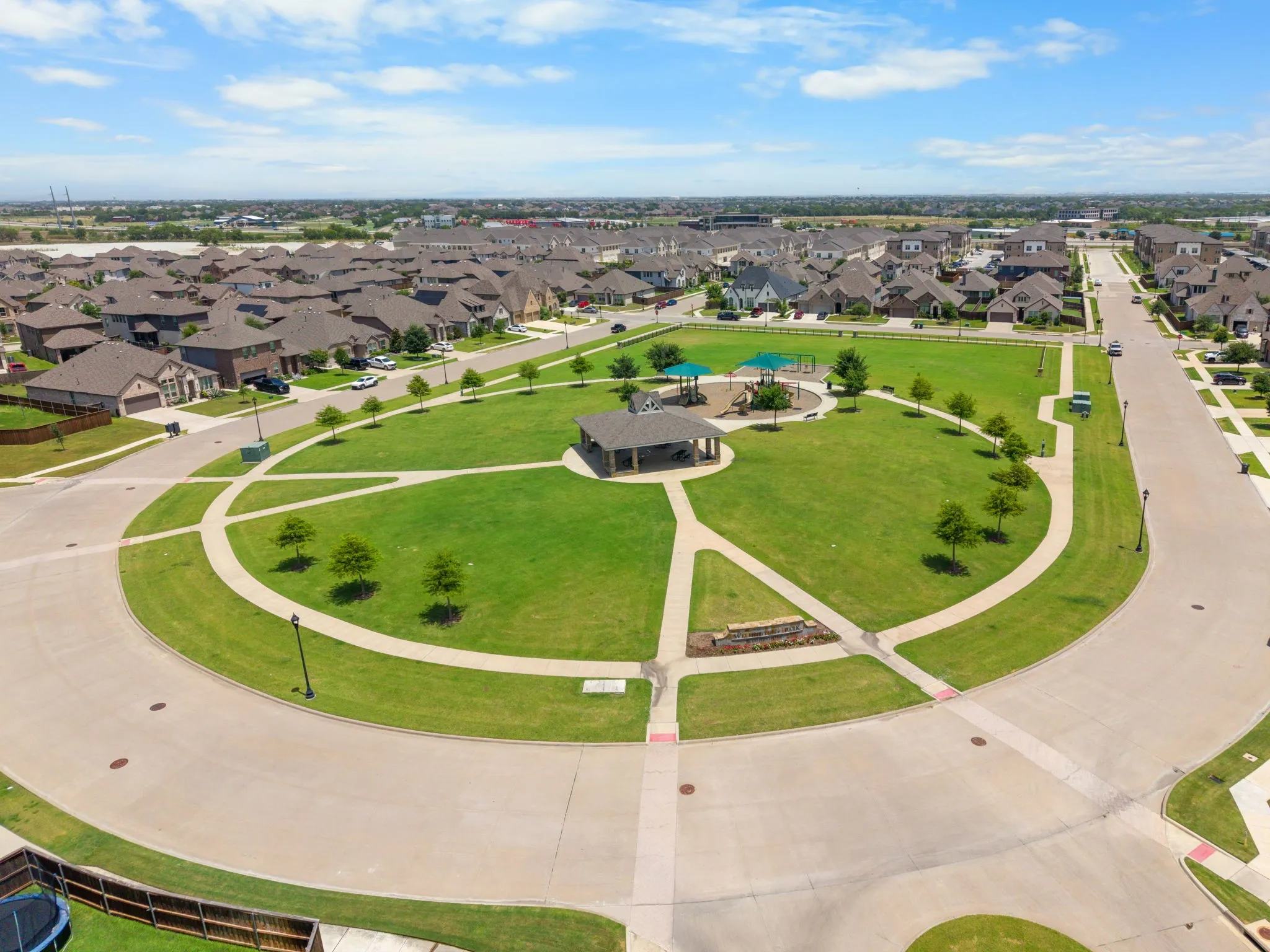 Central community park featuring a green lawn, paved pathways, a covered pavilion, and a playground with shade structures