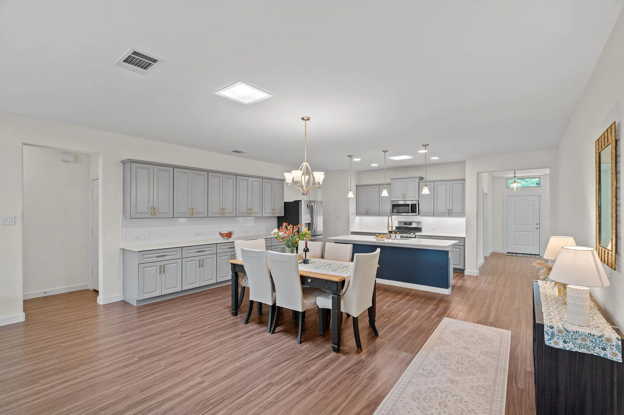 Open-concept living space featuring wood-finish flooring, a contemporary kitchen with light grey cabinetry and a dark blue island, white countertops, and a dining area with chandelier lighting