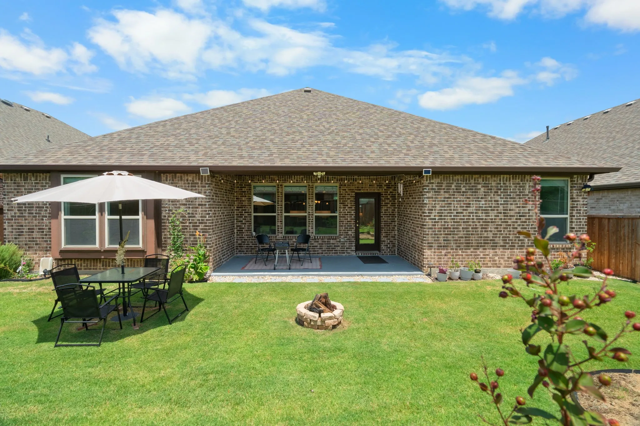 Expansive backyard featuring a manicured lawn, brick exterior, and a covered concrete patio