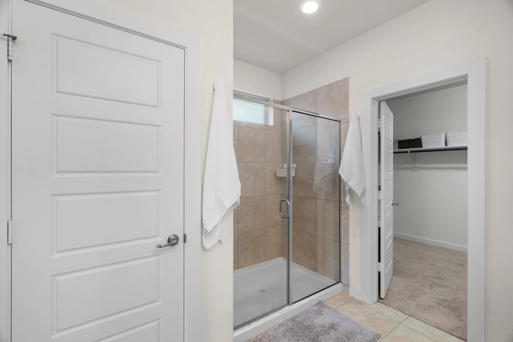 Walk-in shower with clear glass enclosure and light-toned tile surround