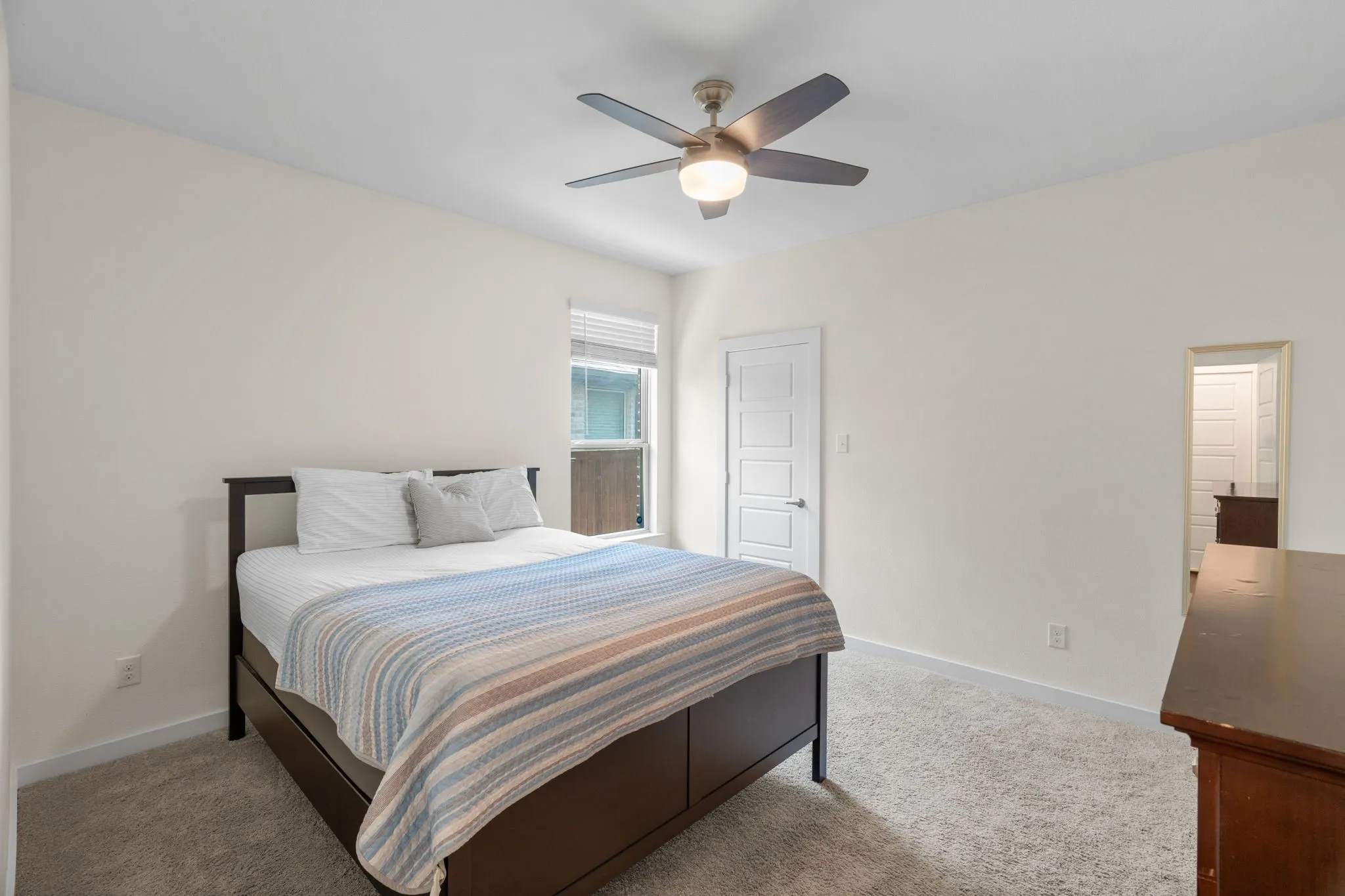 Light-filled bedroom featuring neutral tone walls, soft carpeting, a ceiling fan with integrated lighting, and a white paneled door