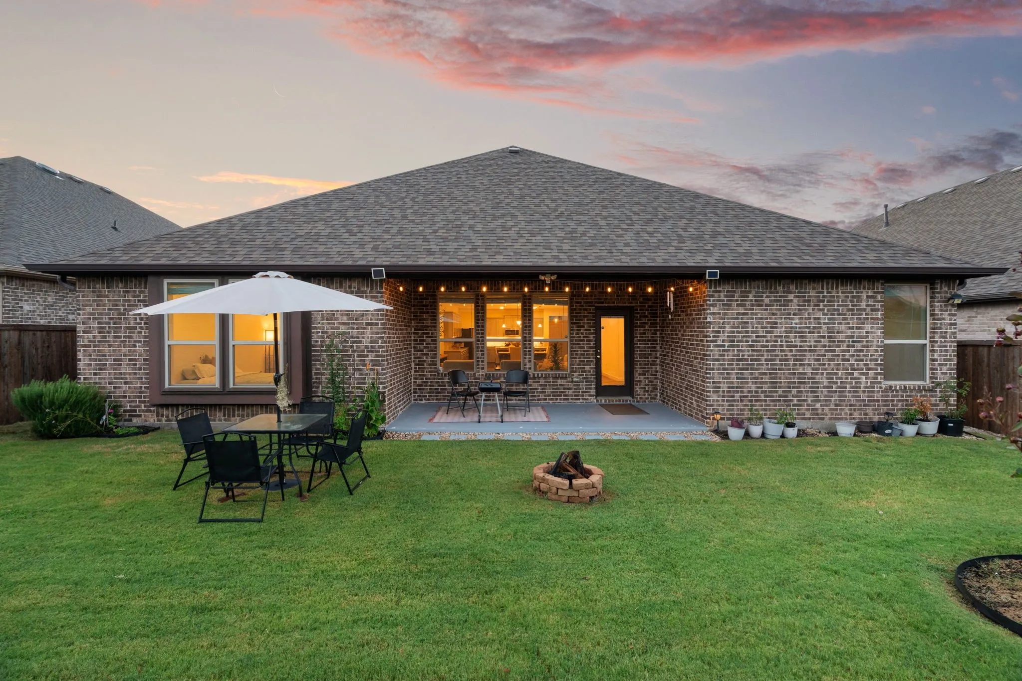 Expansive backyard featuring a manicured lawn, a fire pit area, and a large covered patio