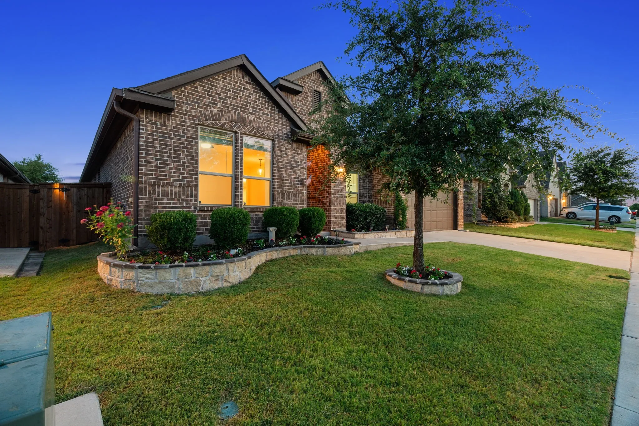 Brick exterior featuring gabled rooflines, a stone-accented planter bed with established shrubbery, a mature front yard tree, and a concrete driveway