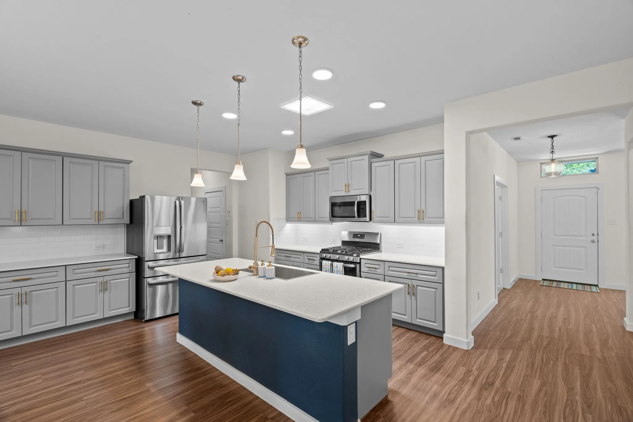 Modern kitchen featuring wood-finish flooring, light gray cabinetry with gold-tone hardware, and a white subway tile backsplash