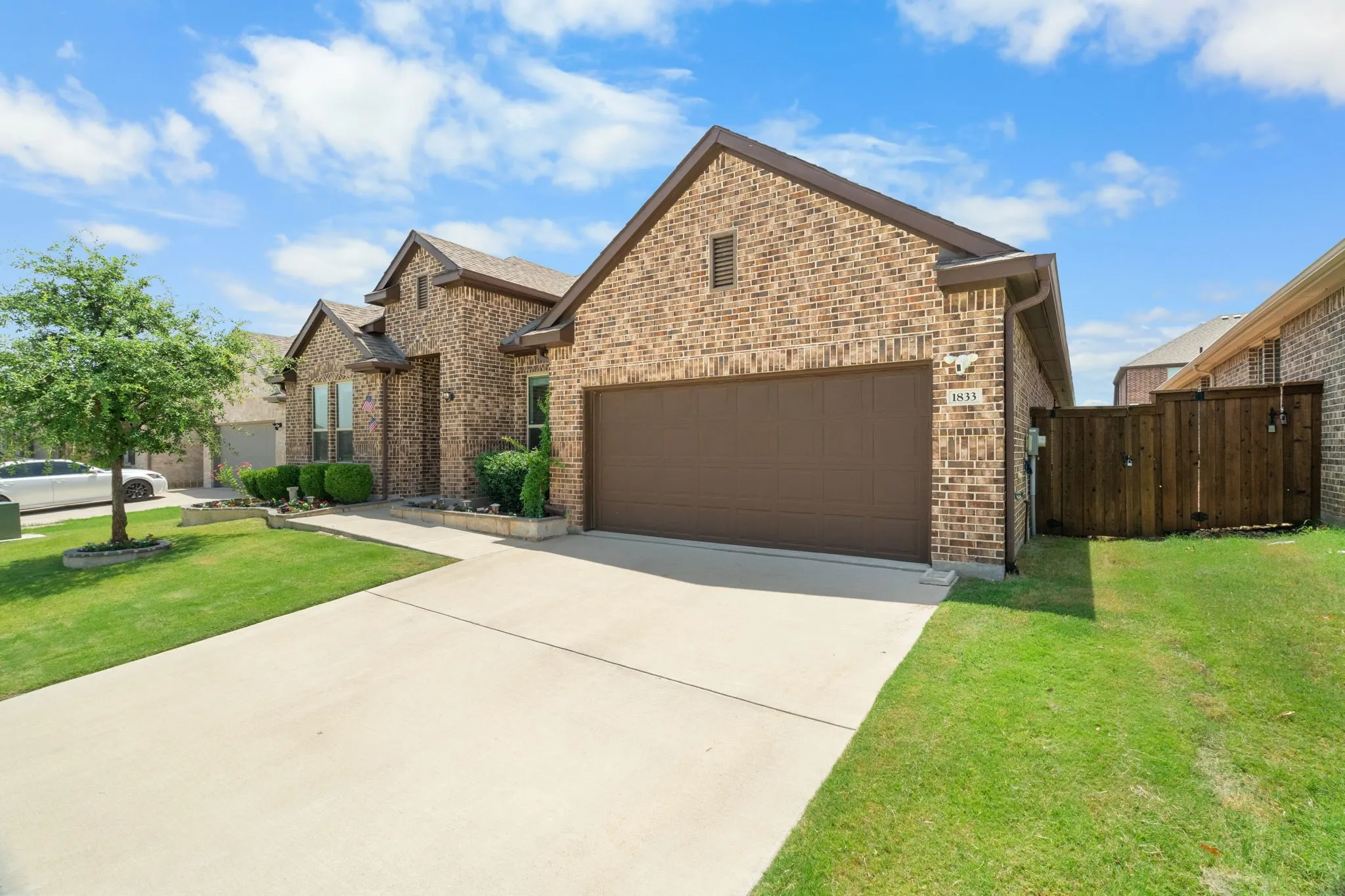 Brick exterior with an attached garage, concrete driveway, and a wood privacy fence