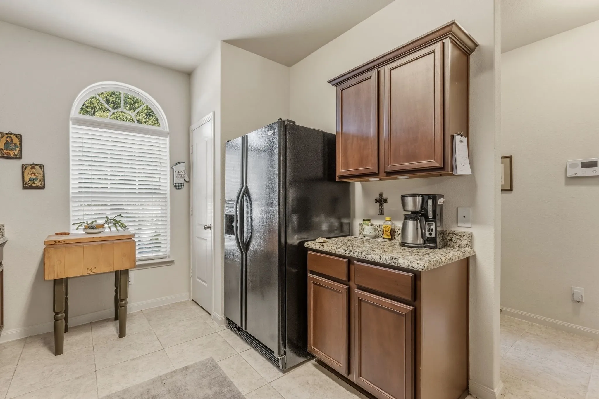 Kitchen area featuring a window with an arched transom, tile flooring, and dark wood cabinetry with a speckled countertop
