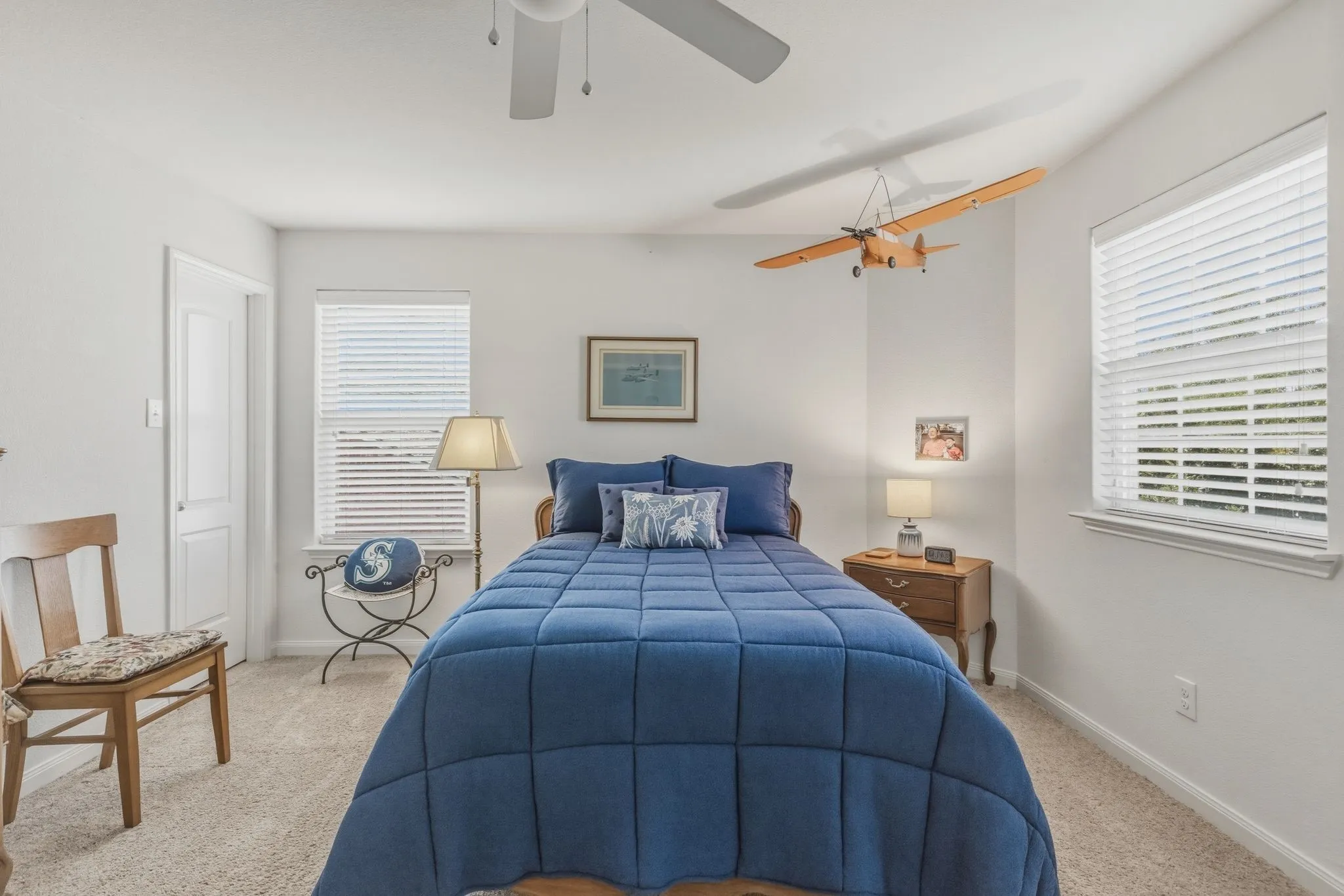 Carpeted bedroom featuring white walls, a ceiling fan, and two windows with horizontal blinds