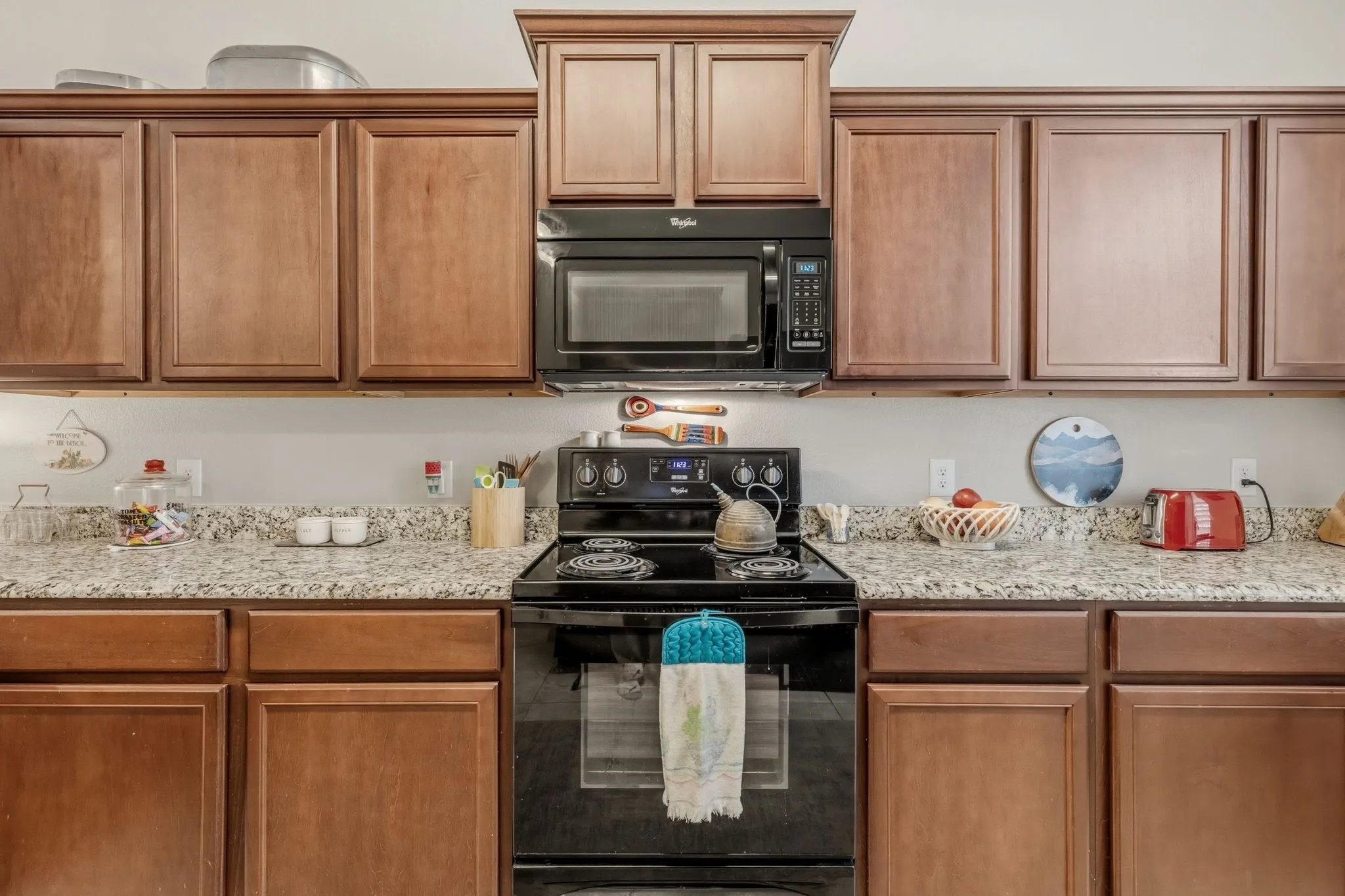 Kitchen featuring wood-finish cabinetry, speckled countertops, a black electric range, and an over-the-range microwave