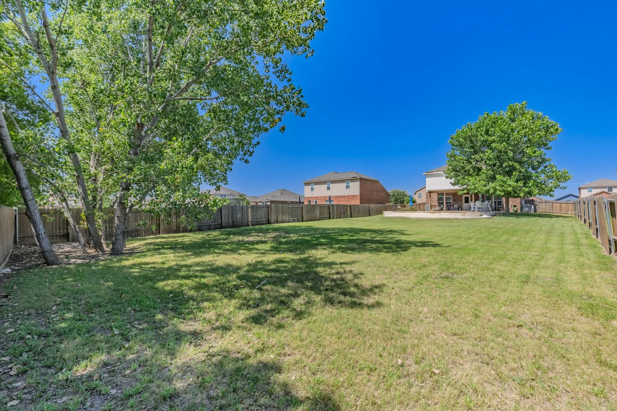 Expansive rear yard featuring a large grass area, mature trees, wood privacy fencing, and a concrete patio