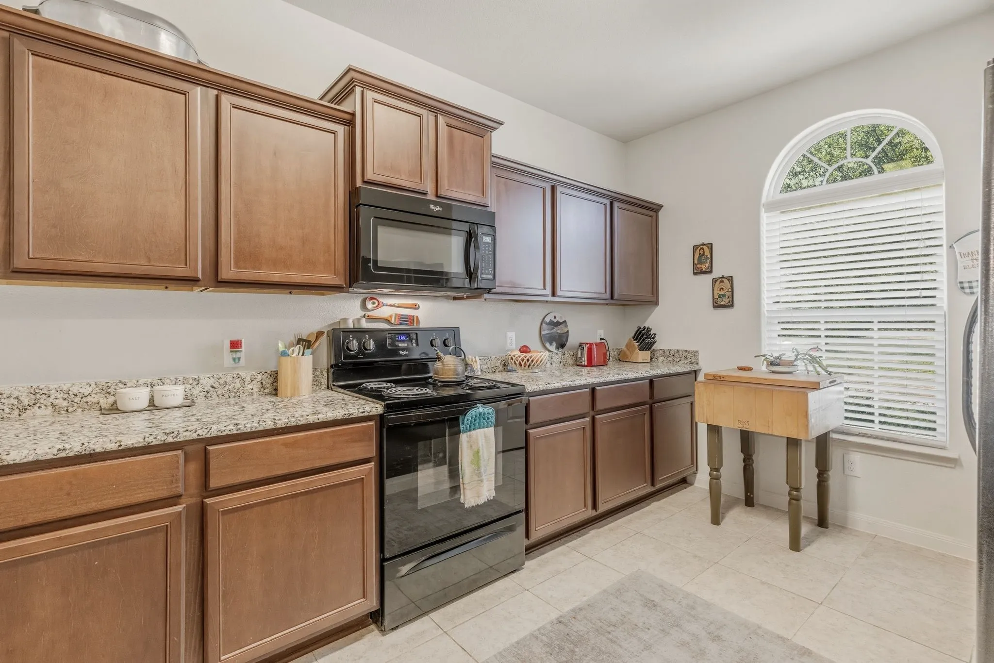 Kitchen featuring wood cabinetry, light-toned countertops, a black range, and a built-in microwave