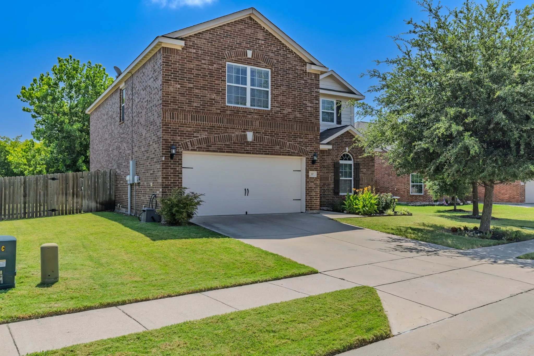 Brick exterior with a two-car garage, mature landscaping, and an arched entry